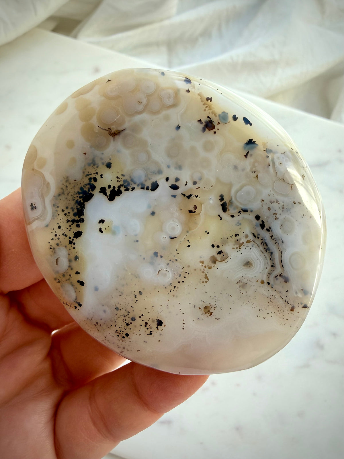 Dendritic Agate crystal held in hand, revealing earthy golden inclusions, black dendritic patterns and polished contours