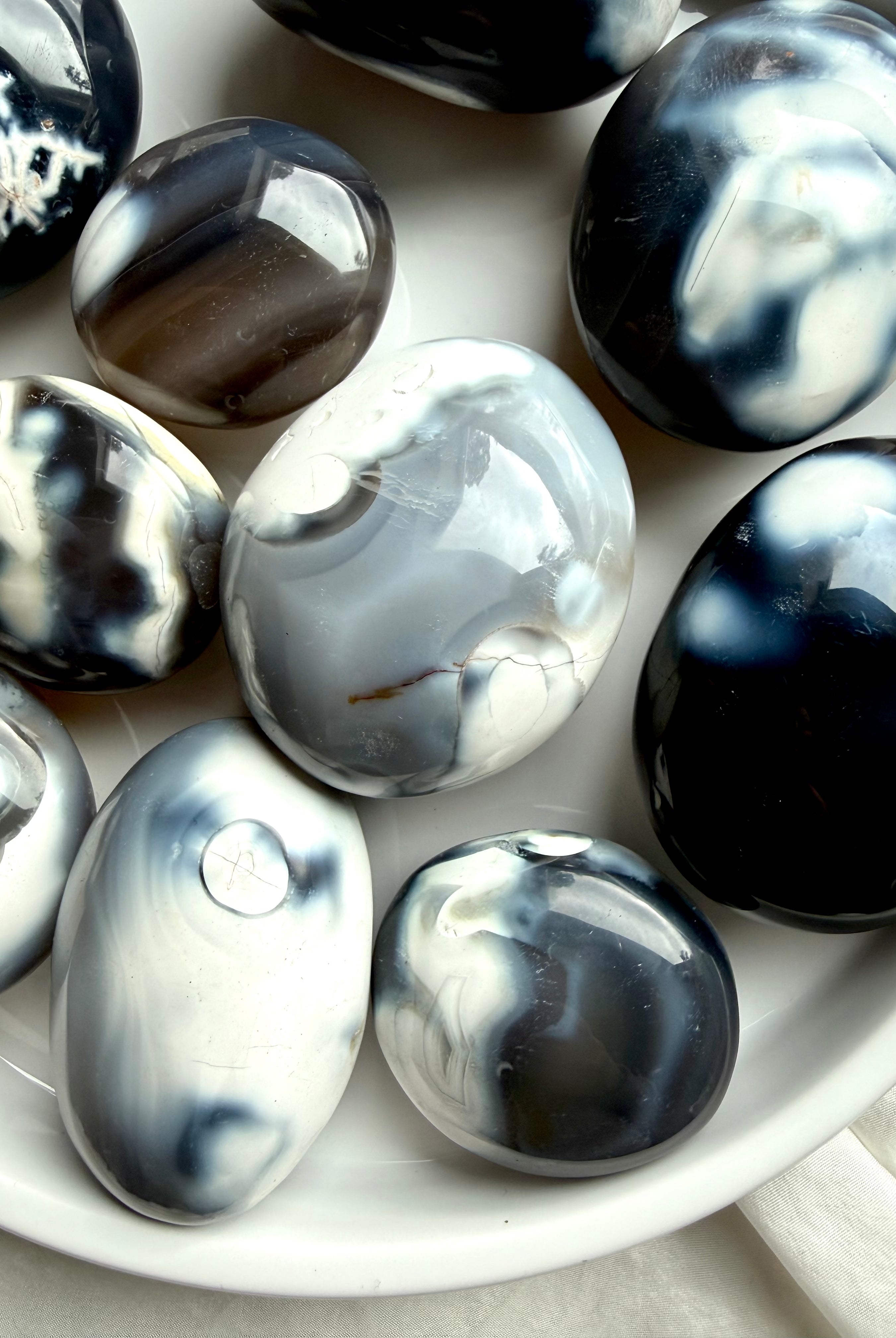 Close-up of Orca Agate palm stones resting in a white tray, showing smooth polish and natural gray, black, and white agate formations