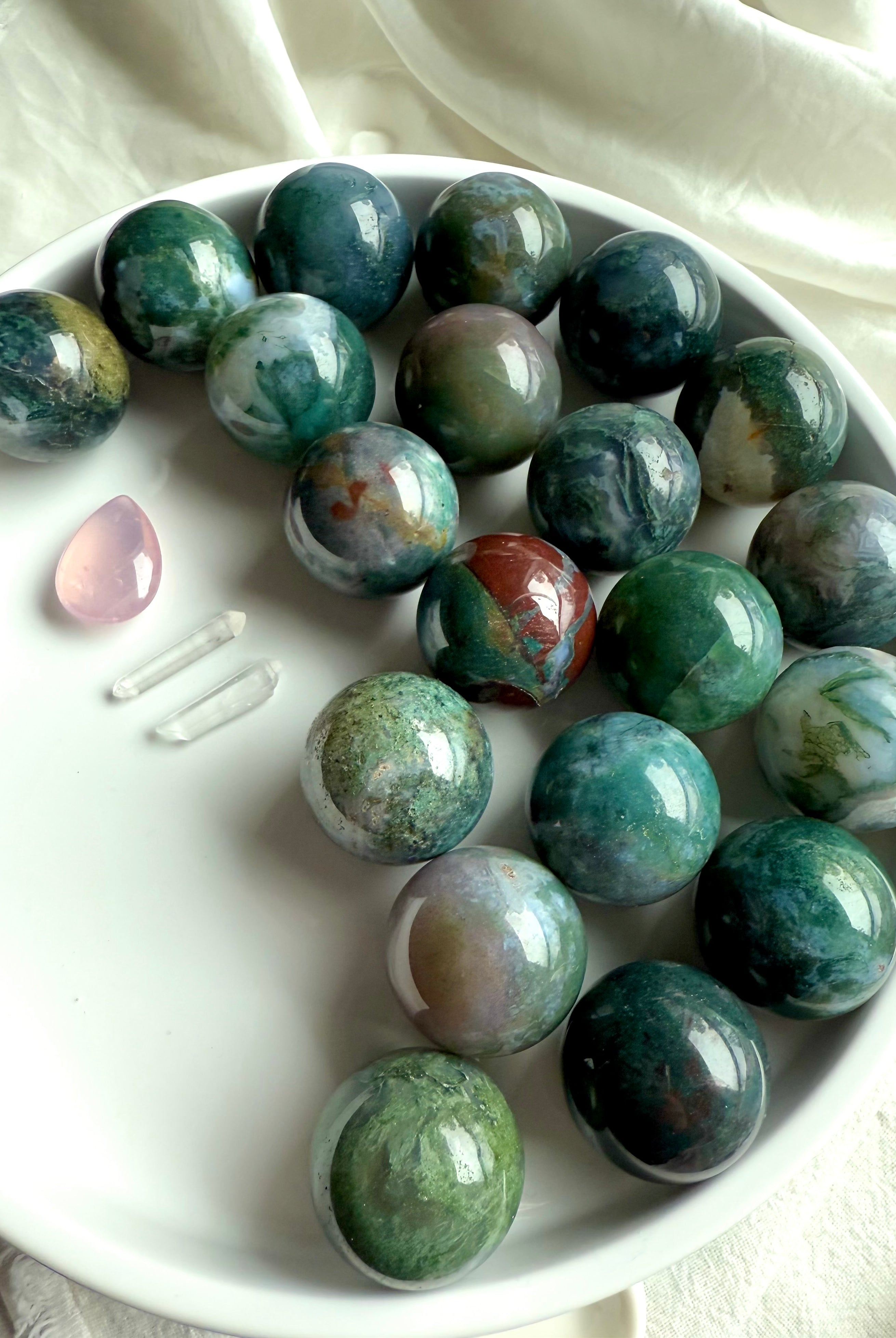Colorful moss agate mini spheres shown on a white plate with some other crystals