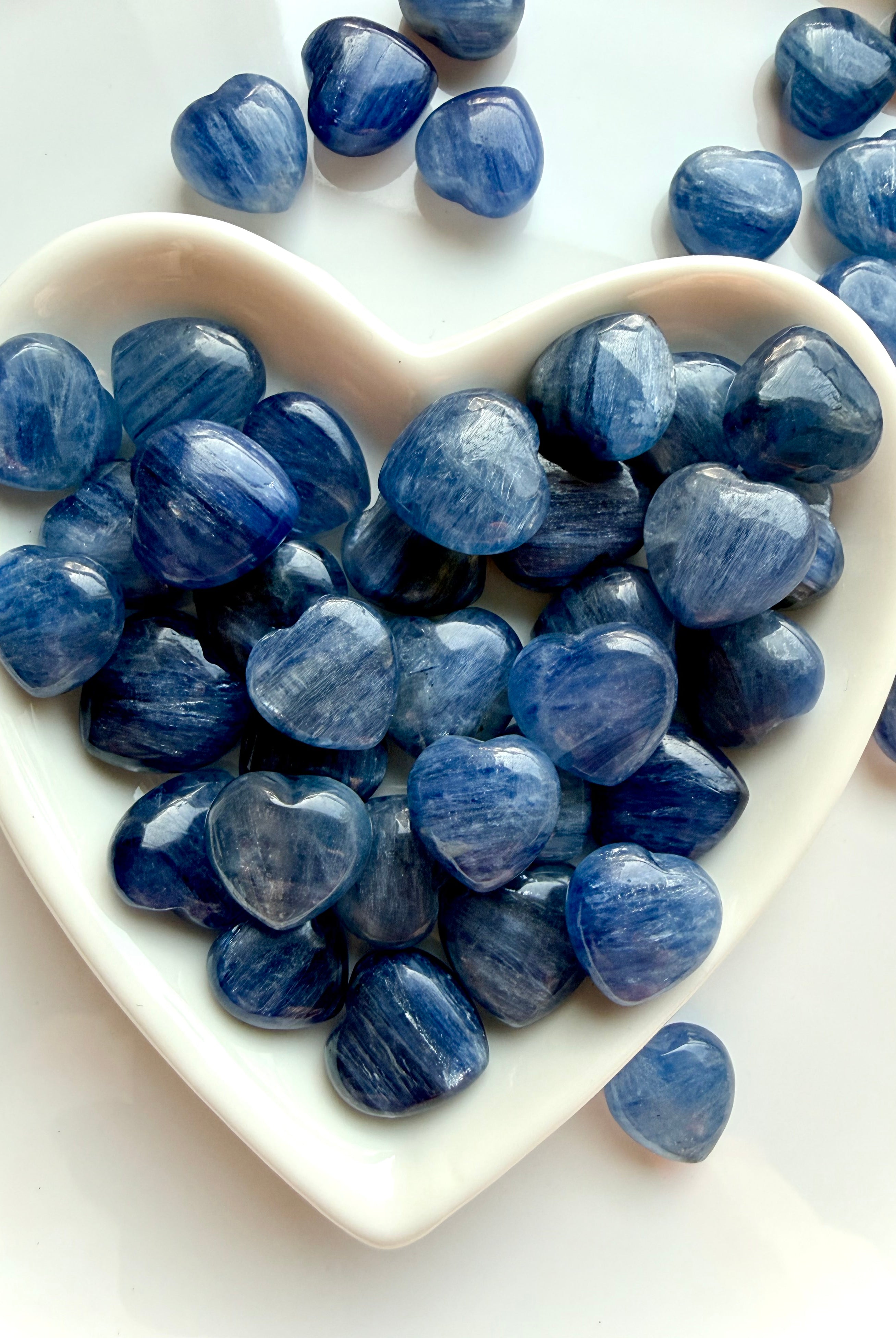 White heart bowl overflowing with mini Blue Kyanite crystal hearts, silvery blue shimmer stones for meditation and chakra healing
