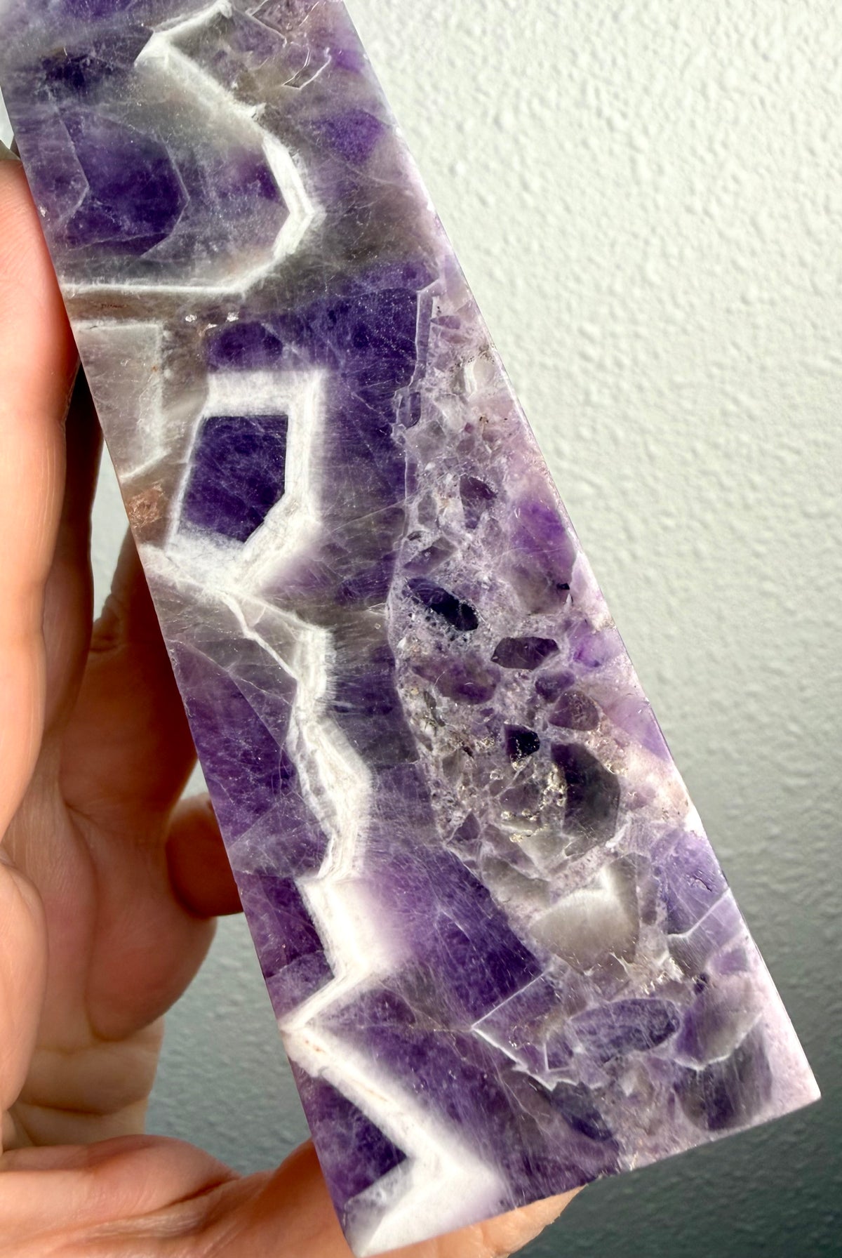 Chevron Amethyst crystal tower held in hand, revealing deep violet formations, intricate white quartz chevrons and natural crystal banding