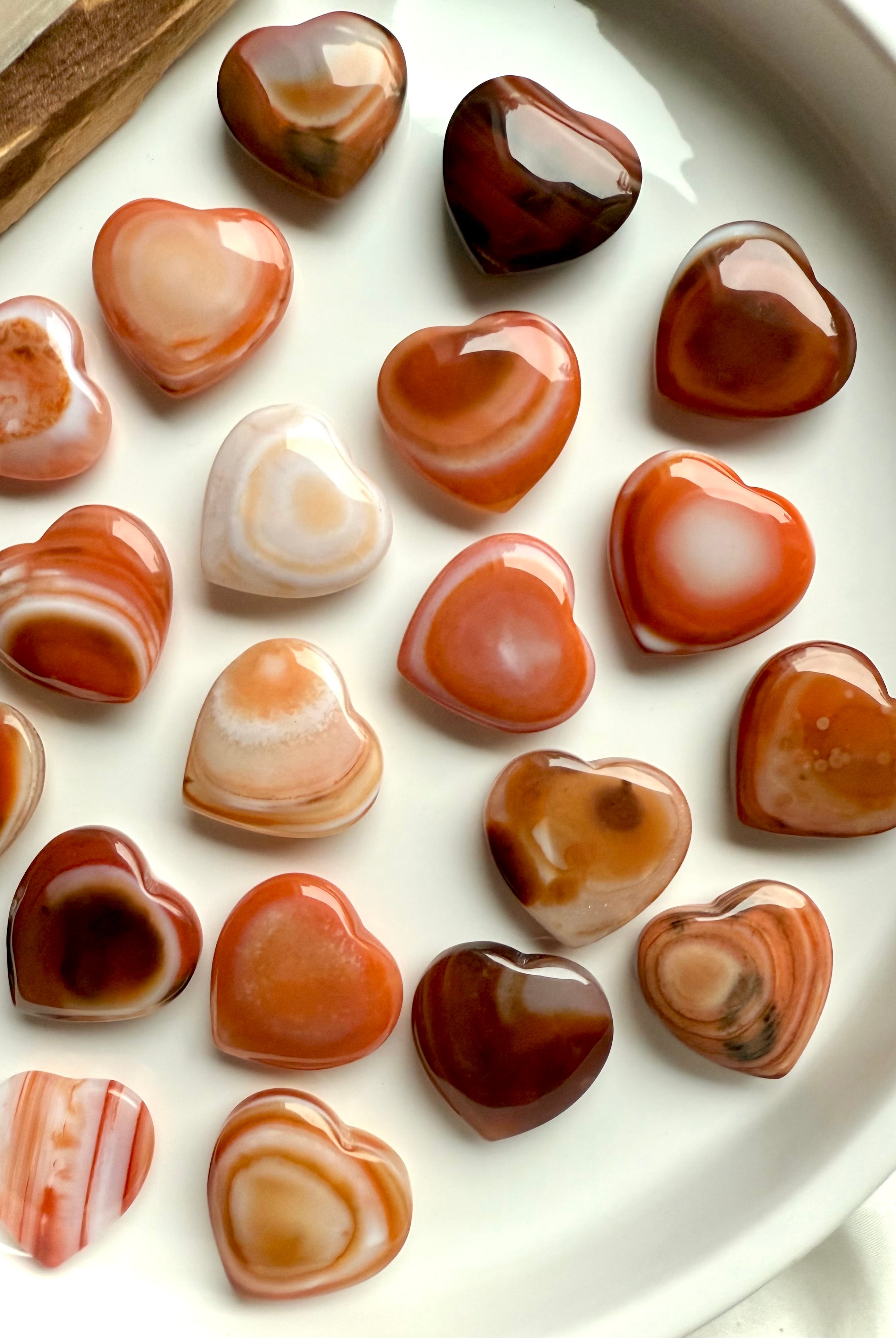Mini Carnelian heart crystals arranged on white tray, showcasing natural banding and warm orange tones for Sacral Chakra healing