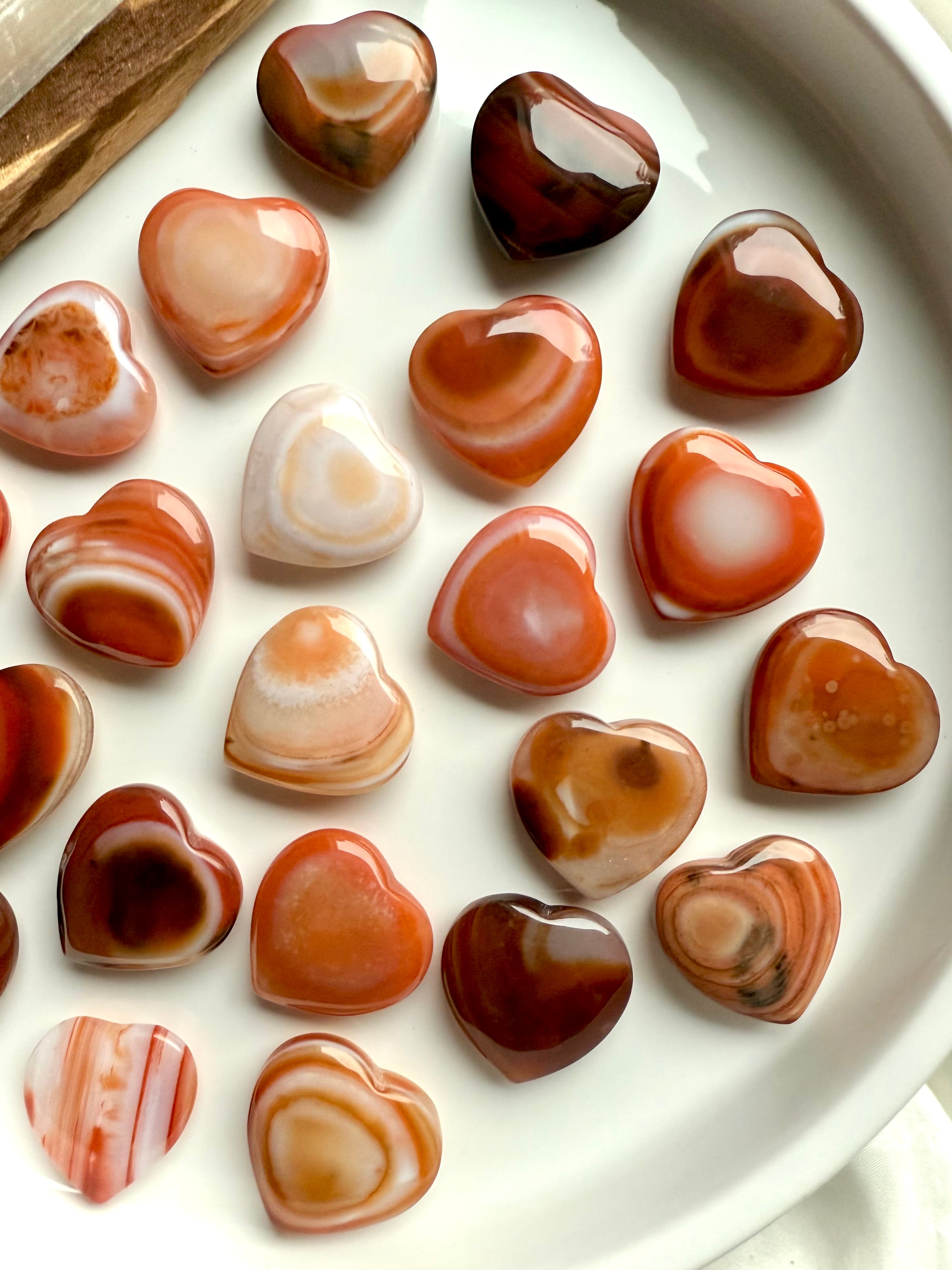 Mini Carnelian heart crystals arranged on white tray, showcasing natural banding and warm orange tones for Sacral Chakra healing