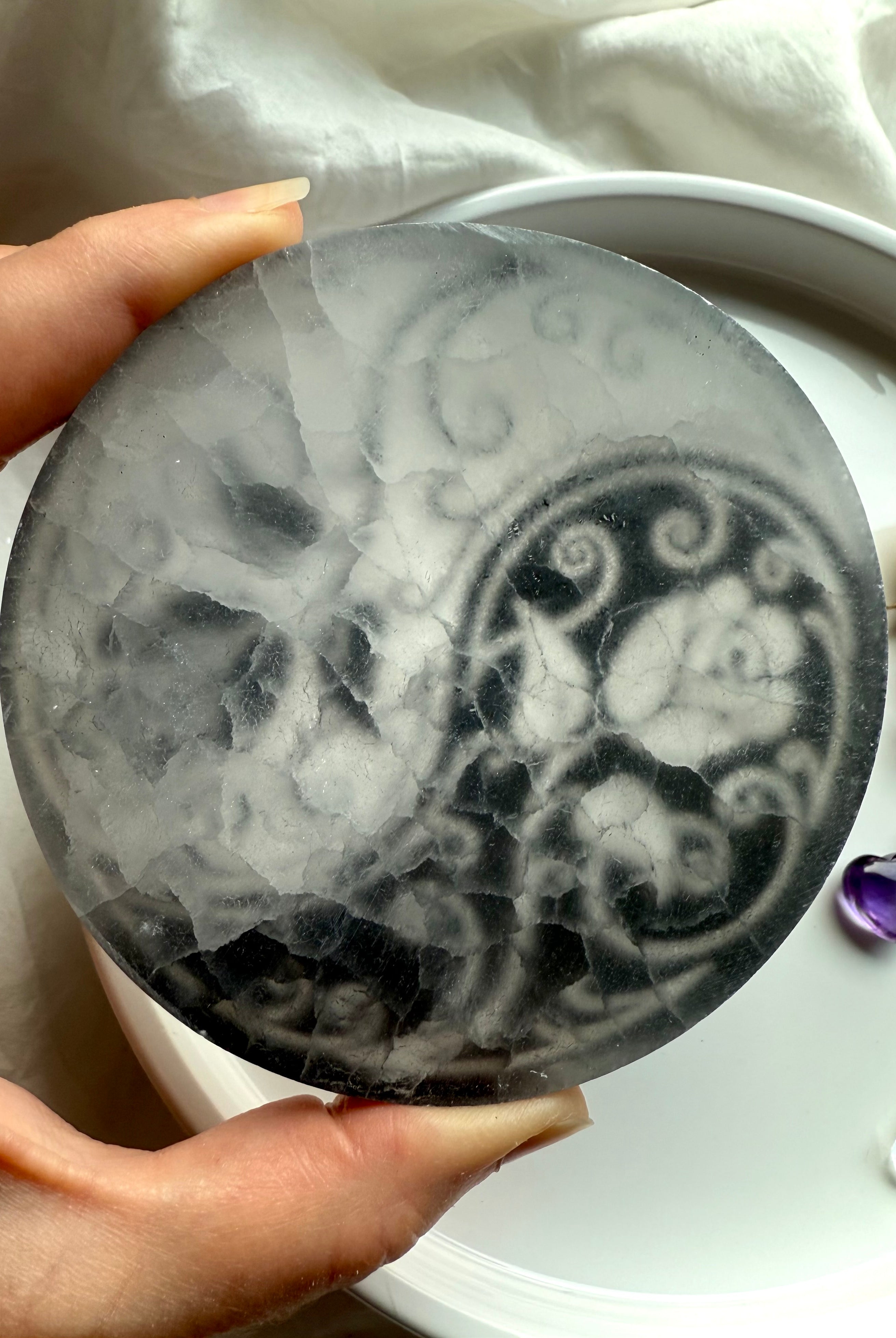 Backside of translucent selenite charging plate showing natural crystal texture and etched yin yang design
