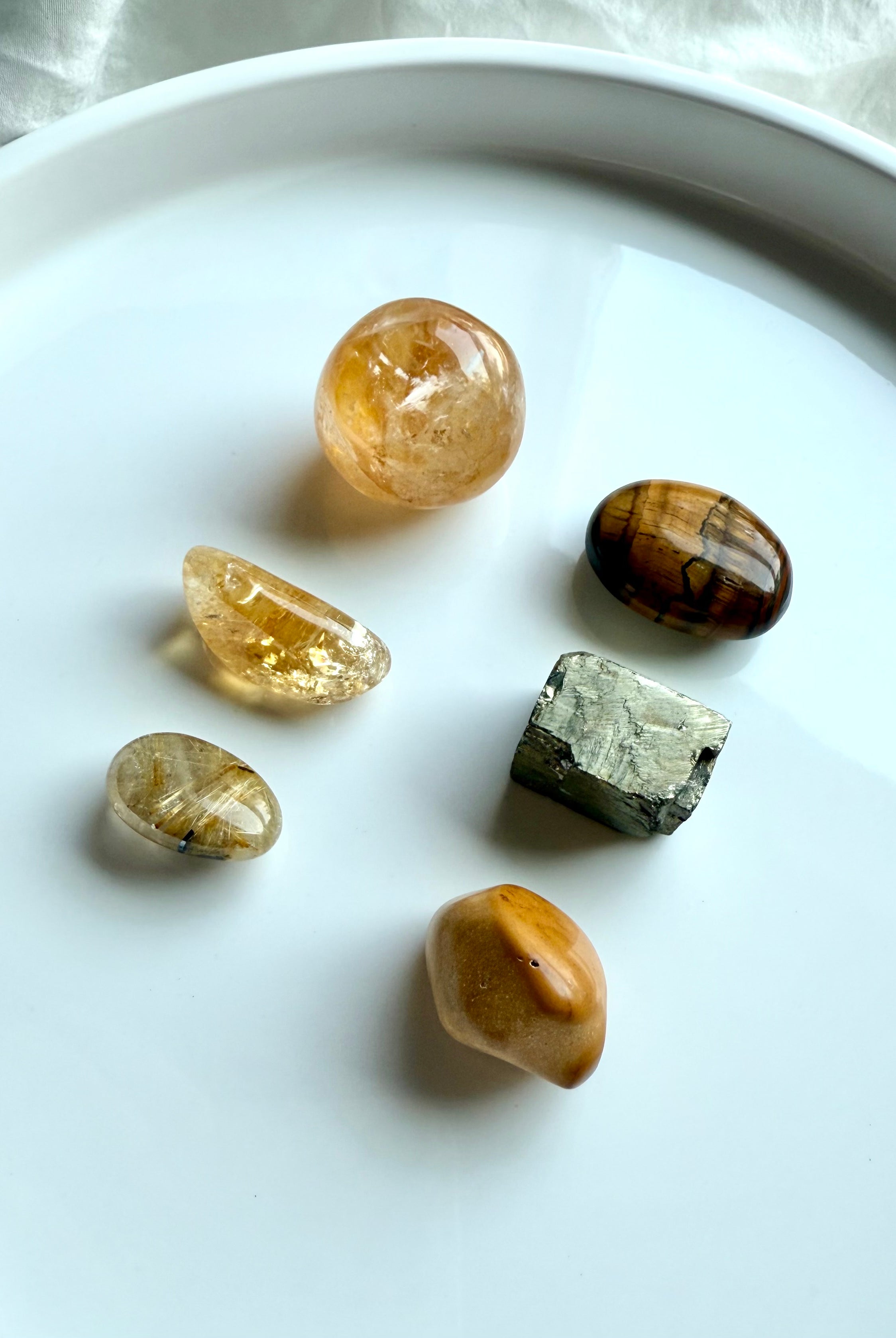 Golden healer, citrine, golden rutile, tiger’s eye, yellow mookaite, and raw pyrite crystals arranged in a grid on white background