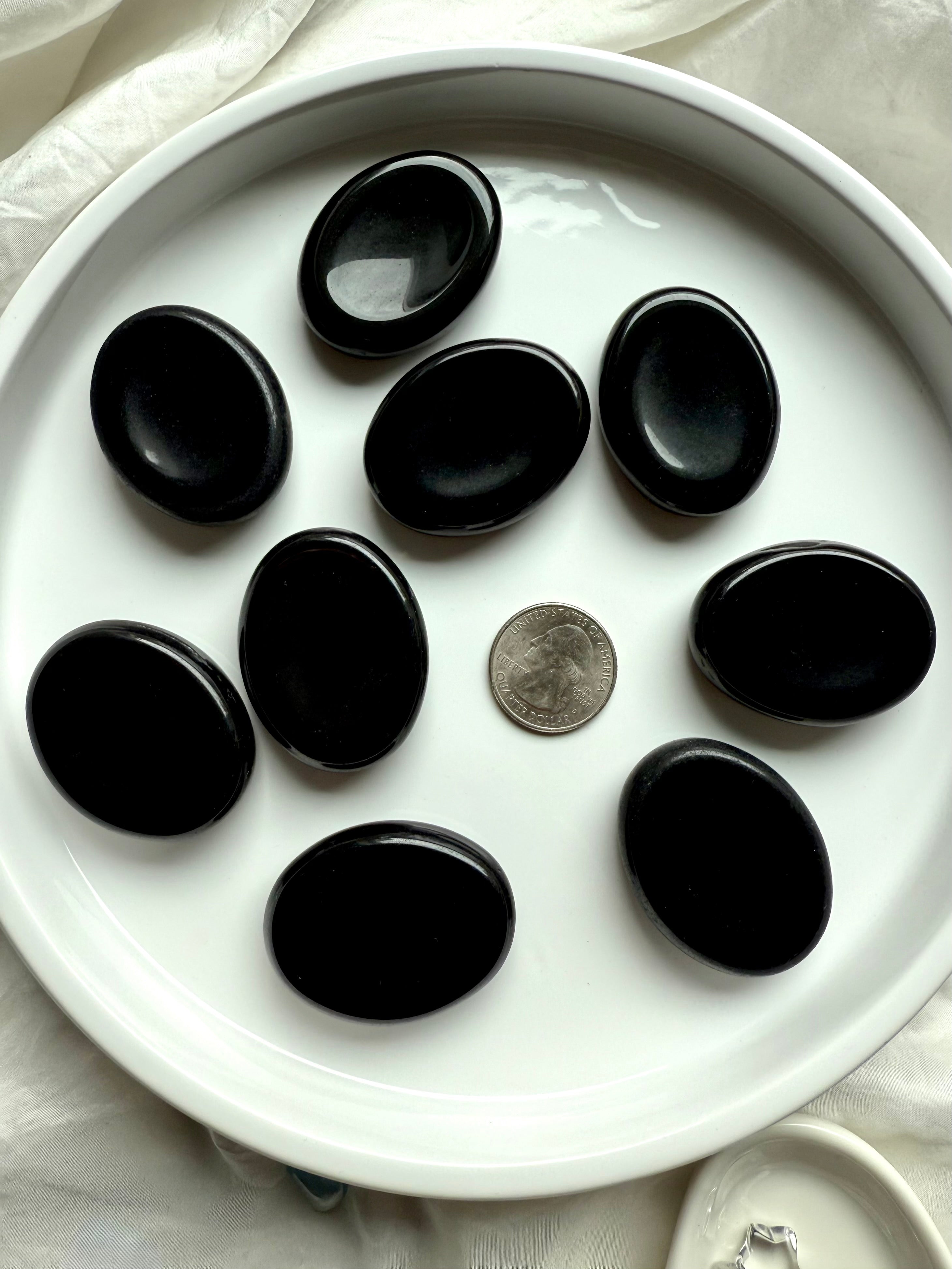 Smooth Black Obsidian worry stones on white tray with US quarter for scale – root chakra healing crystals for stress relief
