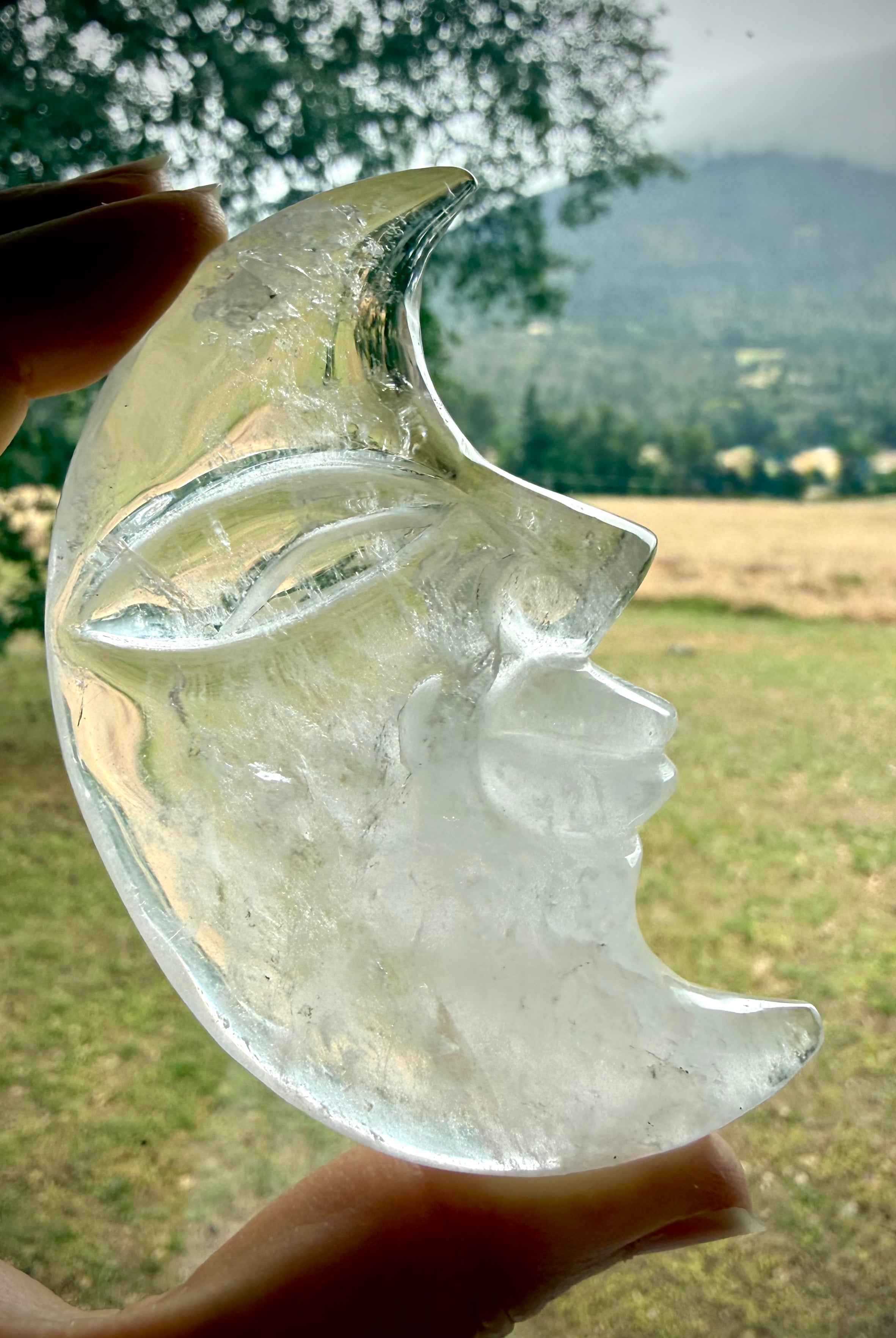 Clear Quartz Moon Face carving glowing in natural light with lovely clarity and detailed celestial crystal craftsmanship
