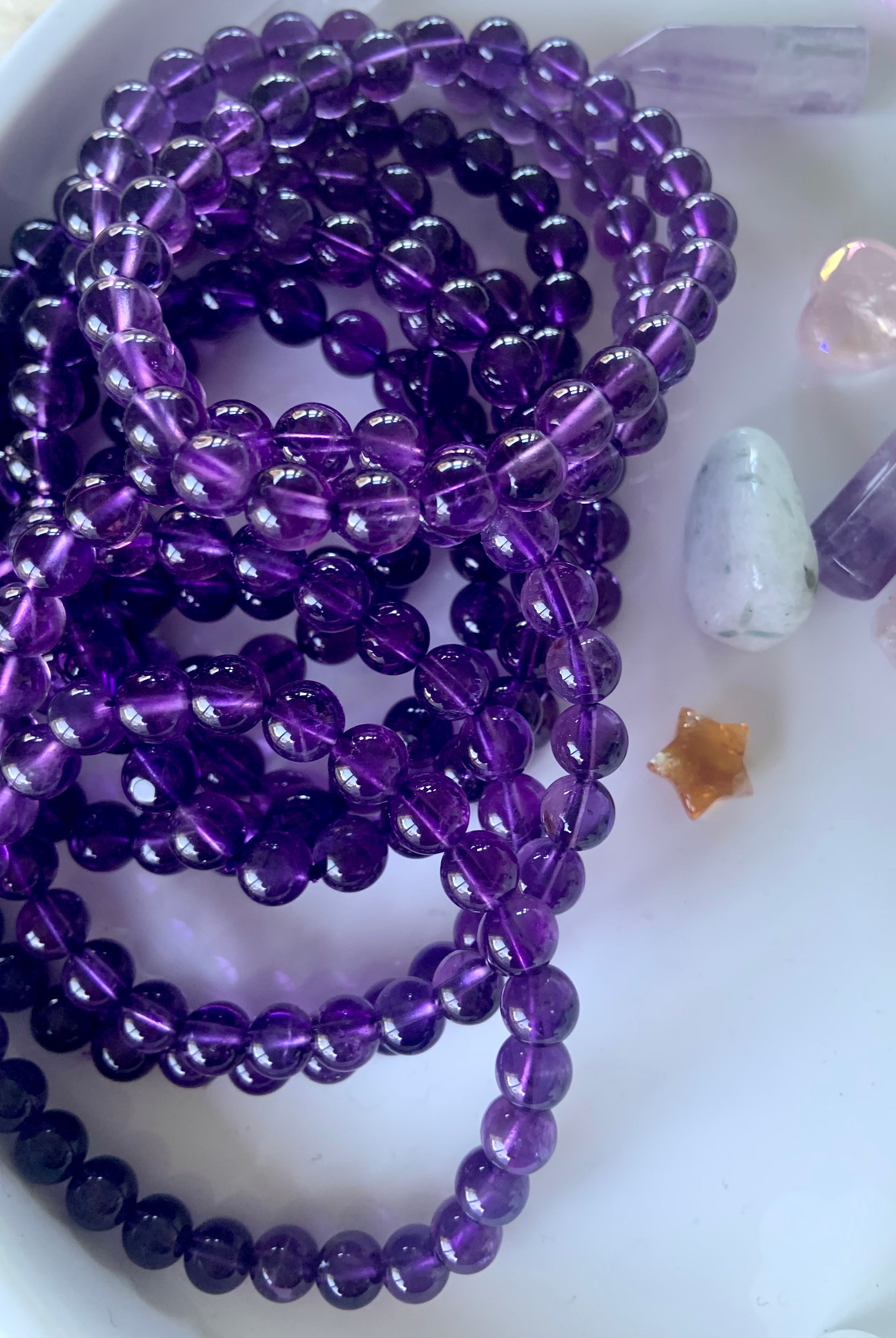 Overhead view of purple amethyst bead bracelets on a white plate with mini crystals in the background