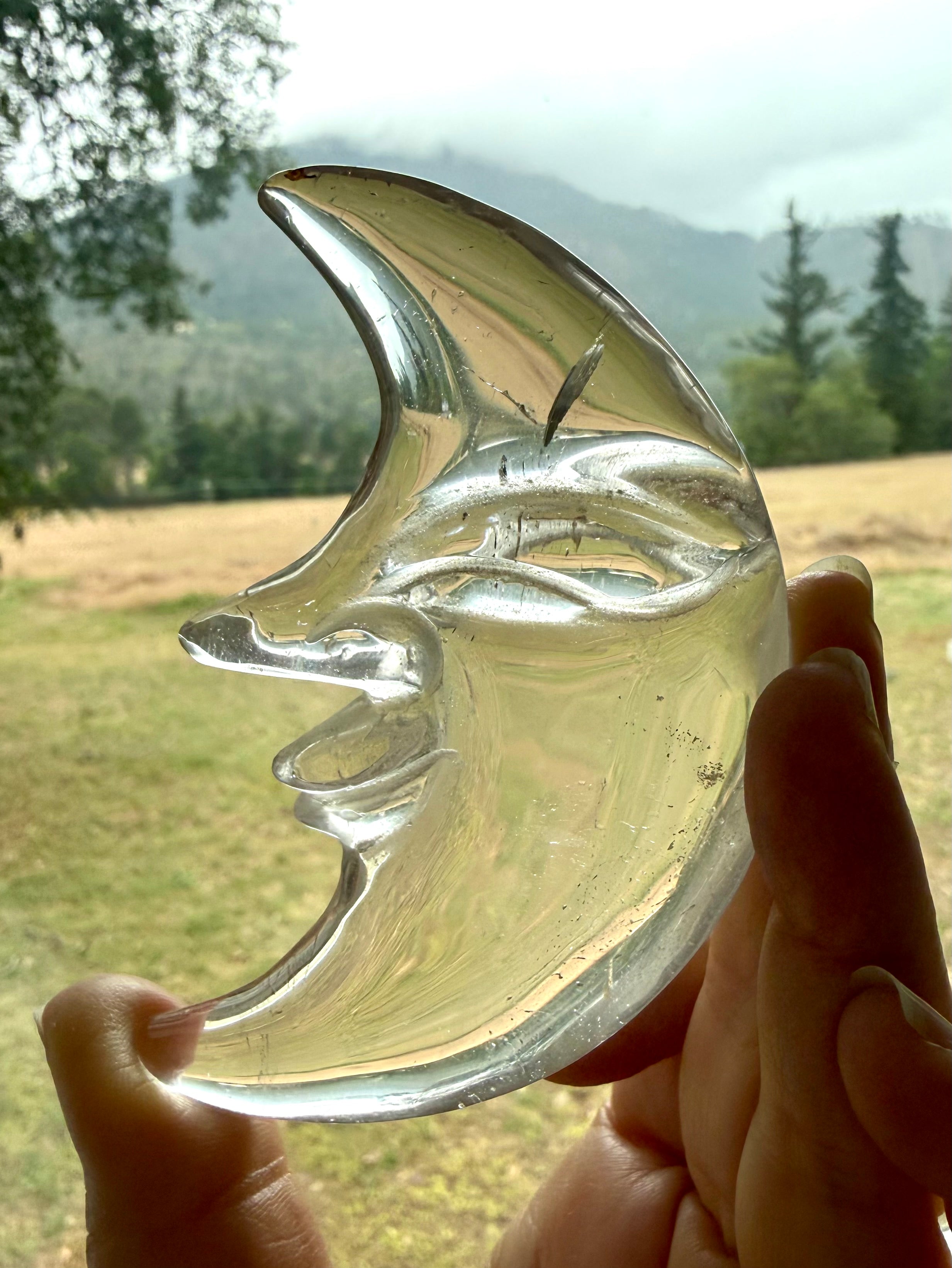 One-of-a-kind Clear Quartz Moon Face carving with a landscape in the background, highlighting remarkable transparency and polished crystal beauty