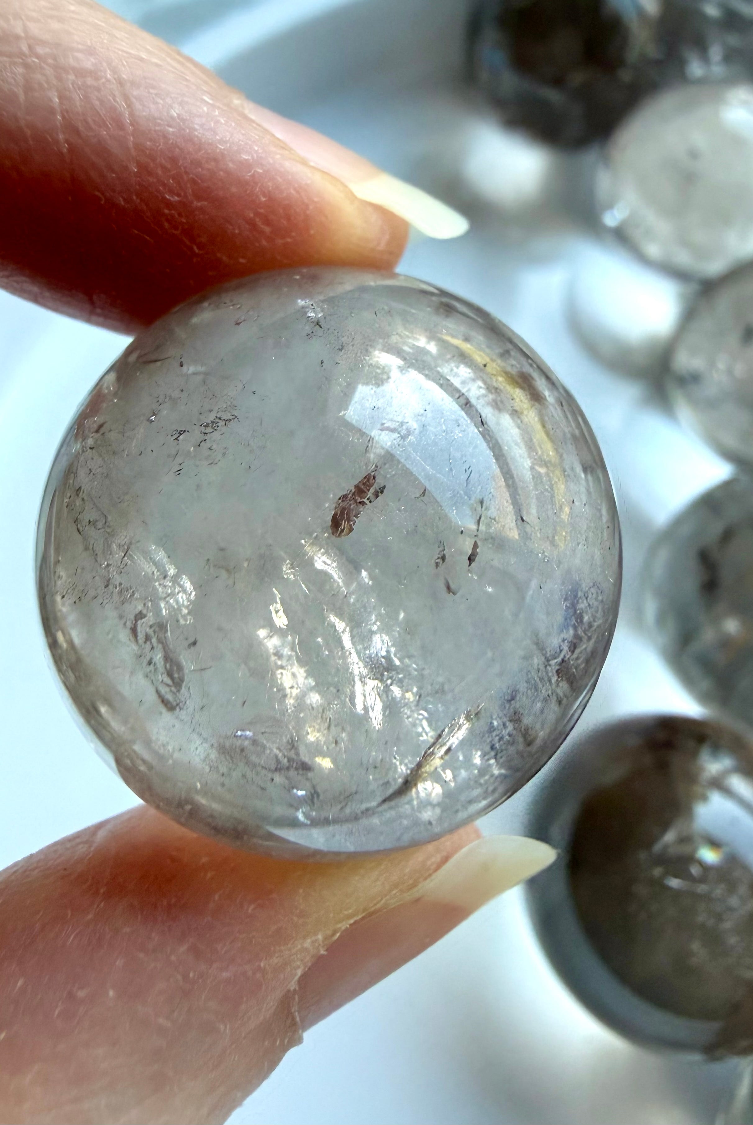 Mini Smoky Quartz crystal sphere close up in hand with internal rainbow flash and natural mineral inclusions