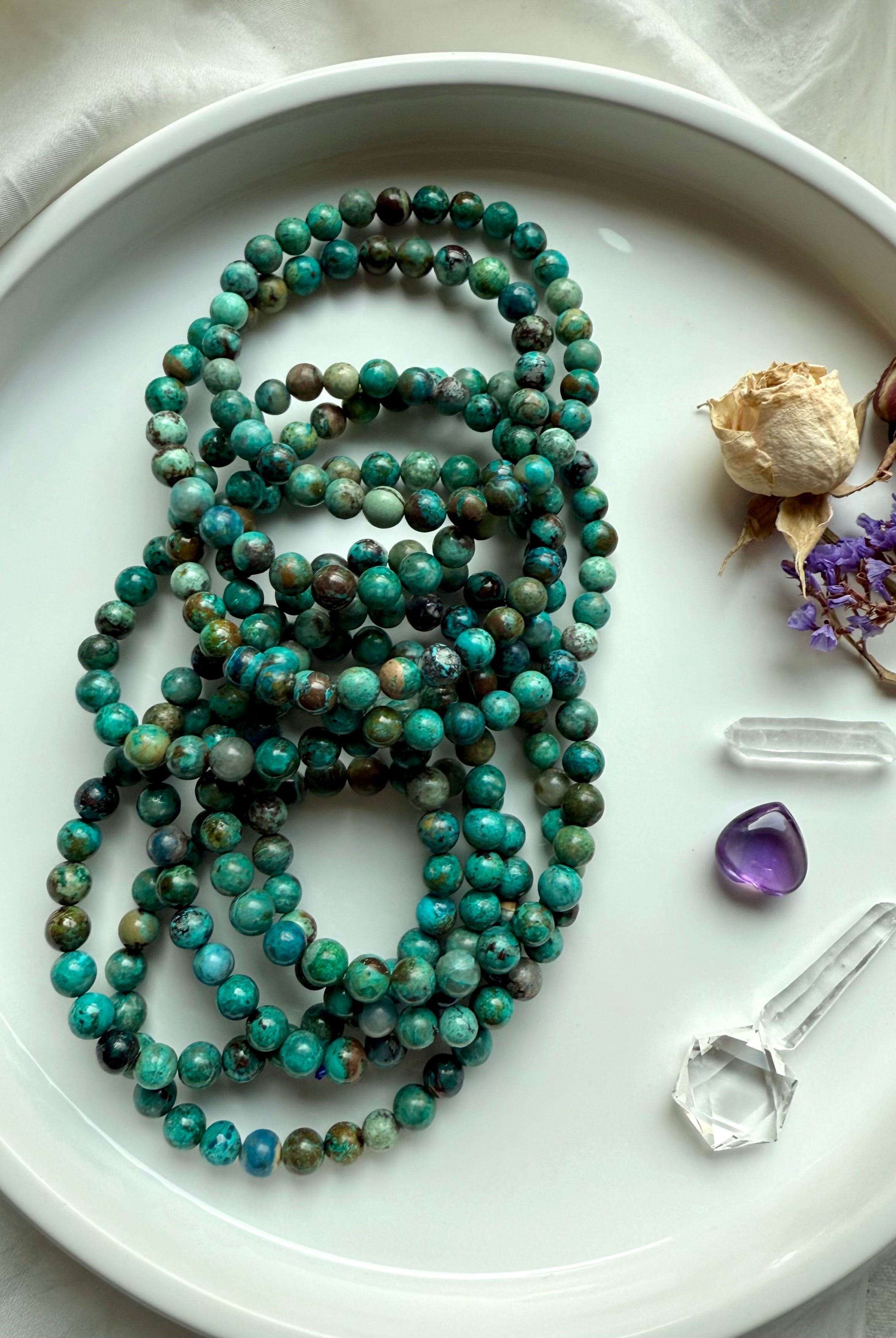 Natural Chrysocolla Shattuckite gemstone bracelets in a pile with vibrant blue-green tones, shown with clear quartz and amethyst crystals