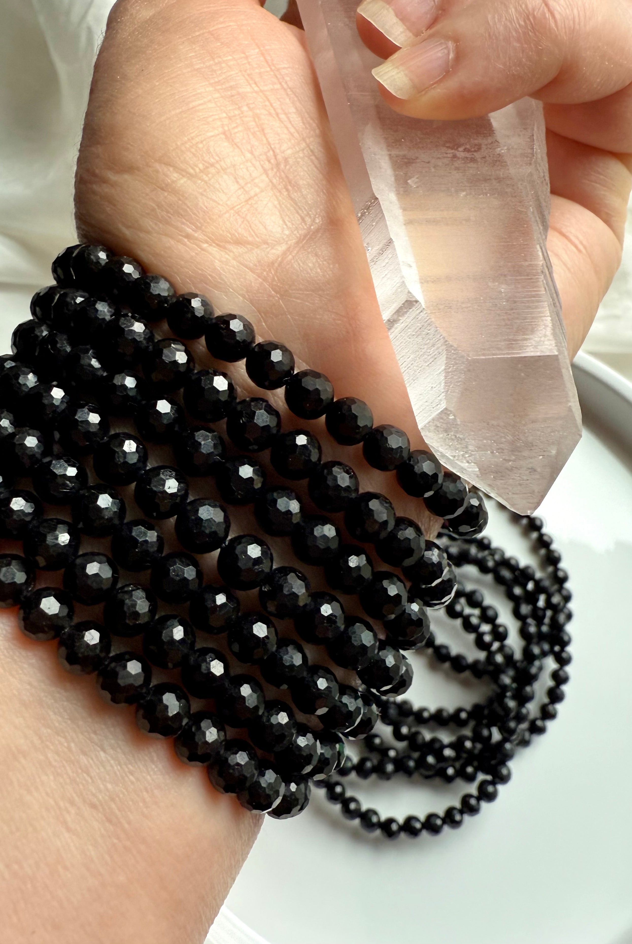 hand holding clear quartz wand with multiple faceted black tourmaline bracelets wrapped around wrist