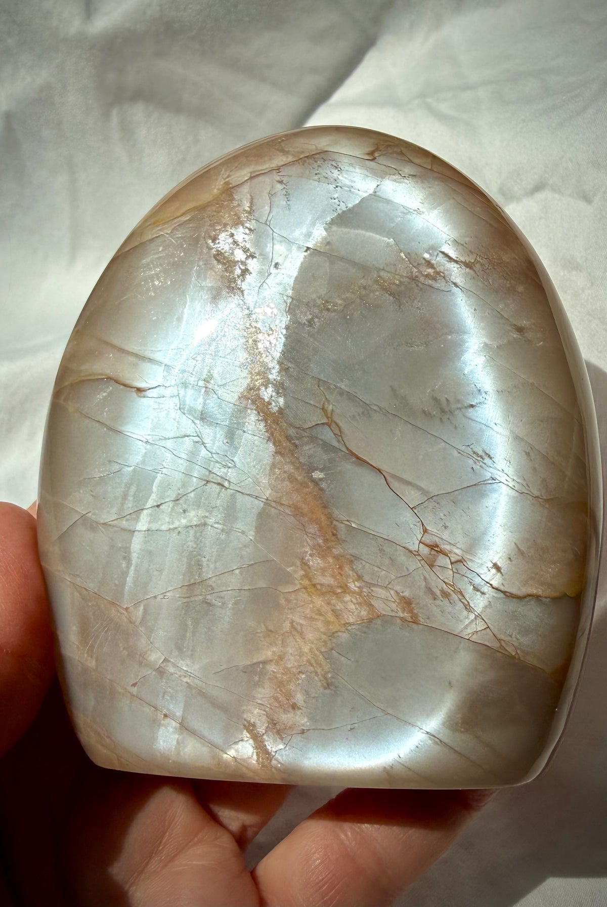Peach Moonstone freeform held in hand showing bright silvery Moonstone glow across the polished face