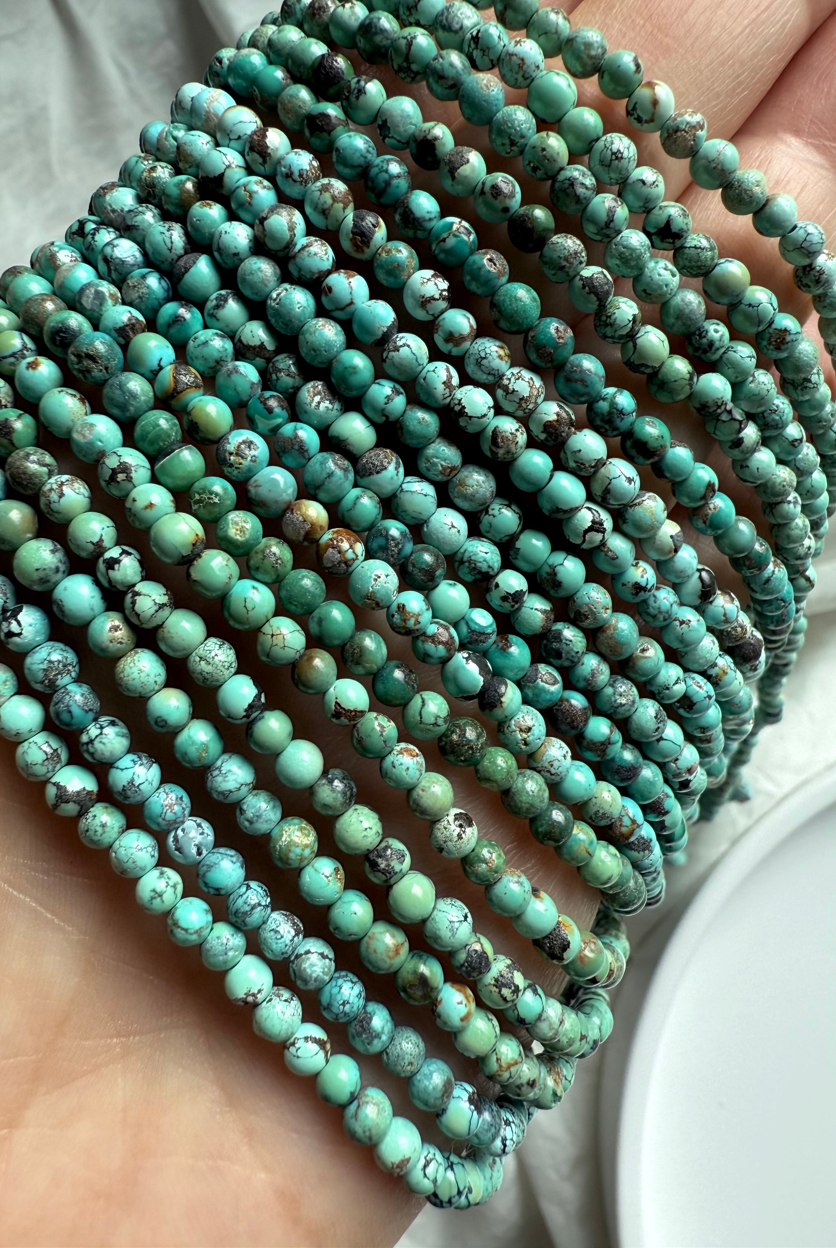 Hand holding multiple Turquoise bead strands with rich green-blue color, organic shapes, and dark matrix lines