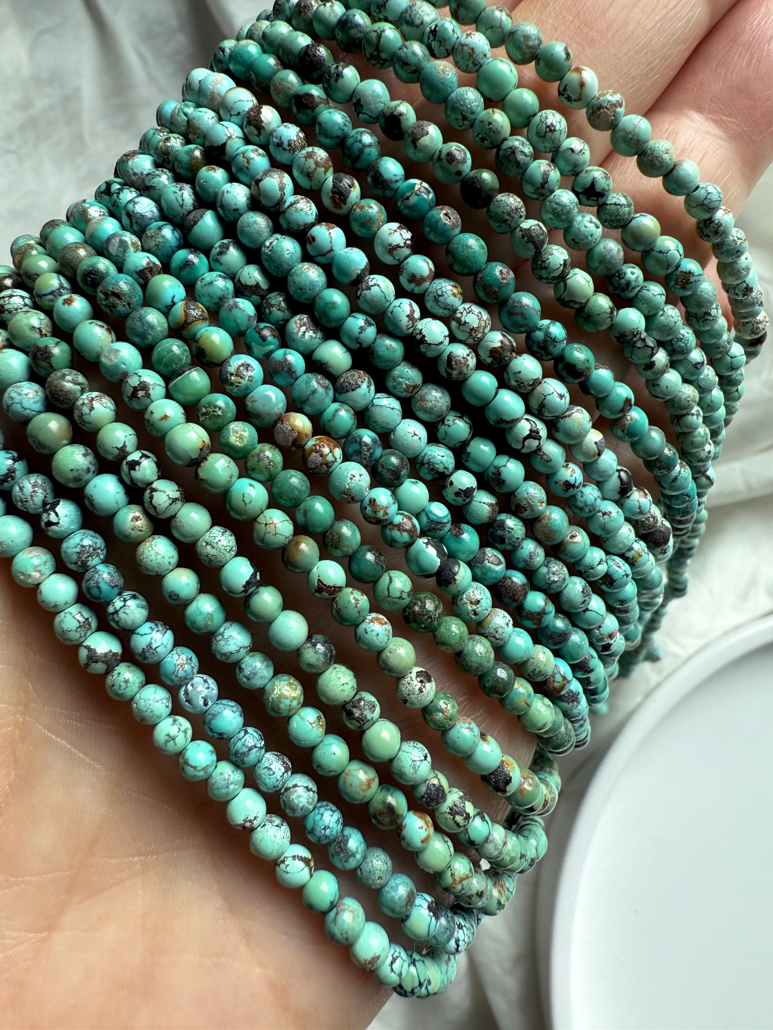 Hand holding multiple Turquoise bead strands with rich green-blue color, organic shapes, and dark matrix lines