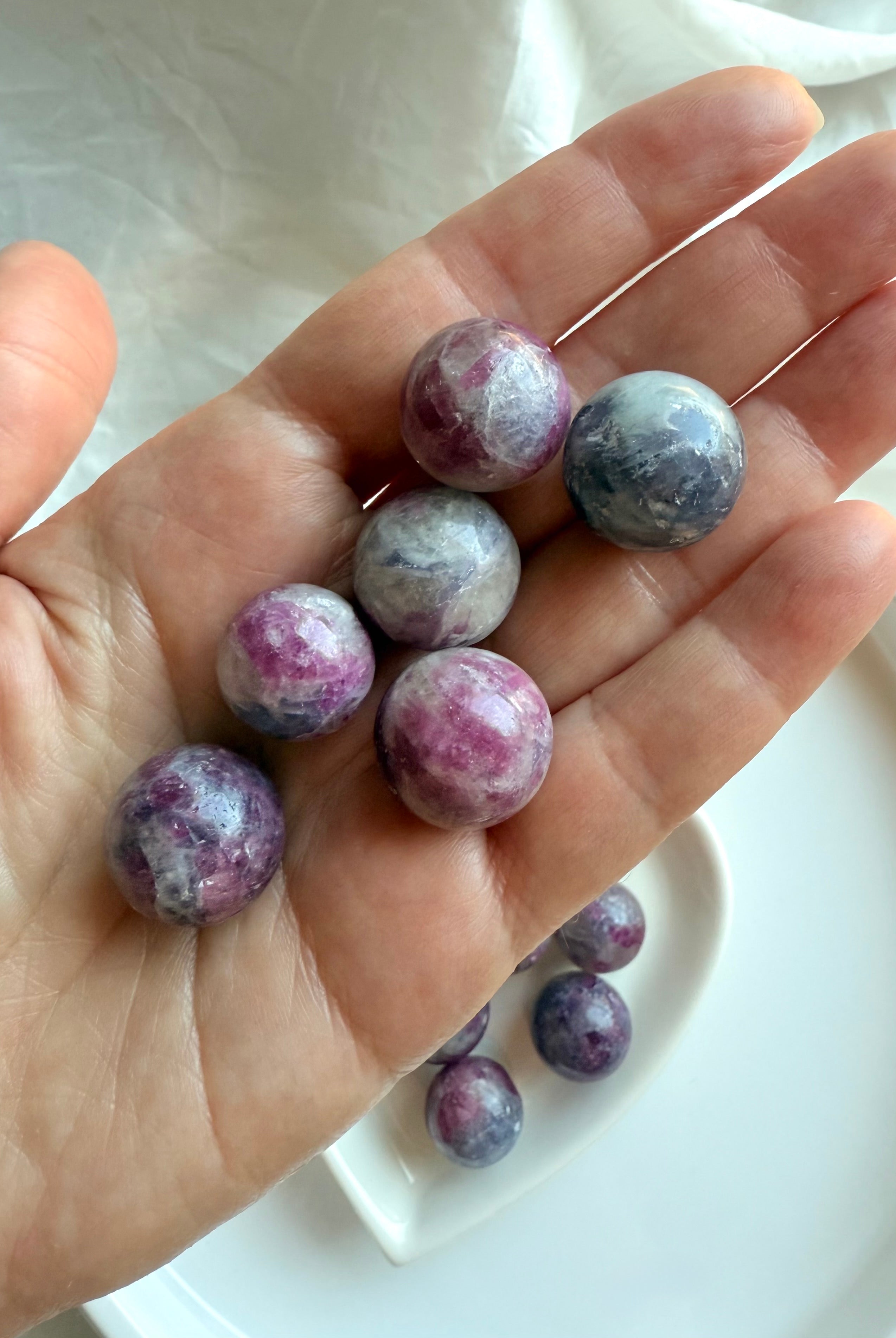 Hand holding several polished Mini Unicorn Stone spheres showing natural pink, purple, and gray tones
