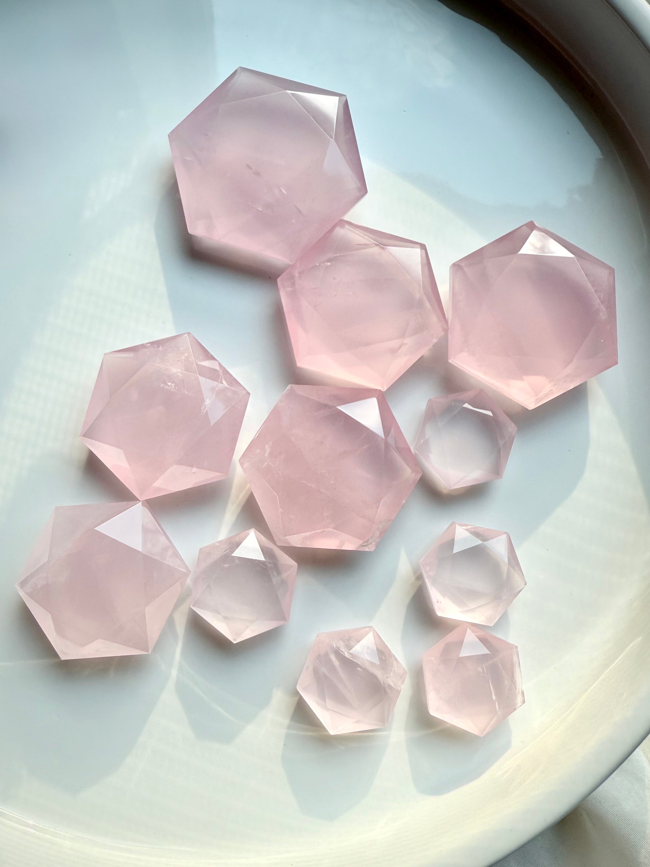 Close-up of polished rose quartz hexagon crystals in varied sizes, faceted pink stones for crystal grids and sacred décor.