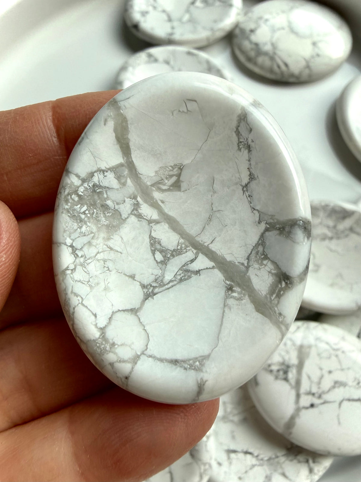 Howlite worry stone held between fingers showing polished surface, gray veining and calming tactile thumb indentation