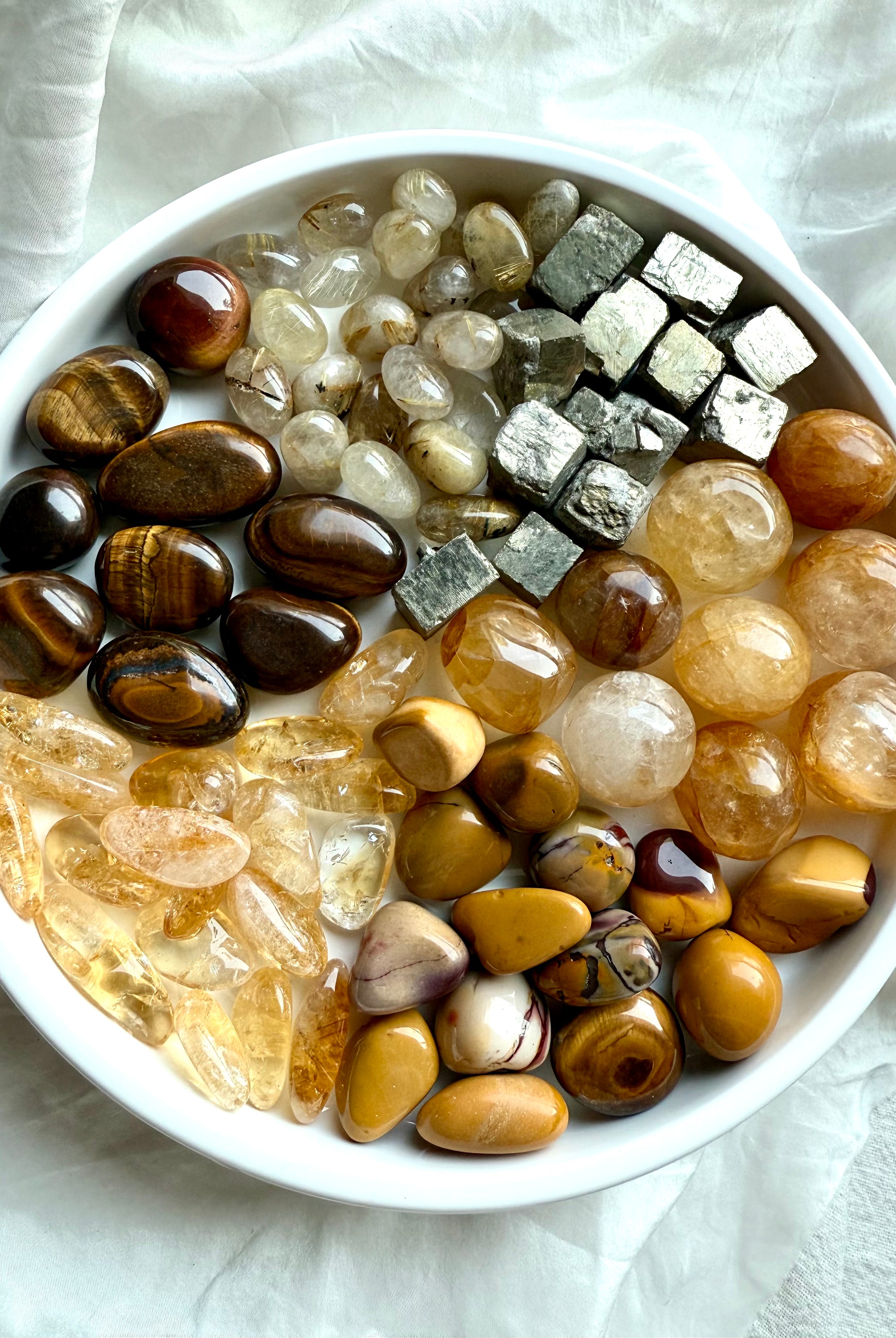 Solar Plexus Chakra crystals arranged in segmented pie slices on a white plate — golden healer, citrine, golden rutile, tiger’s eye, yellow mookaite, and raw pyrite