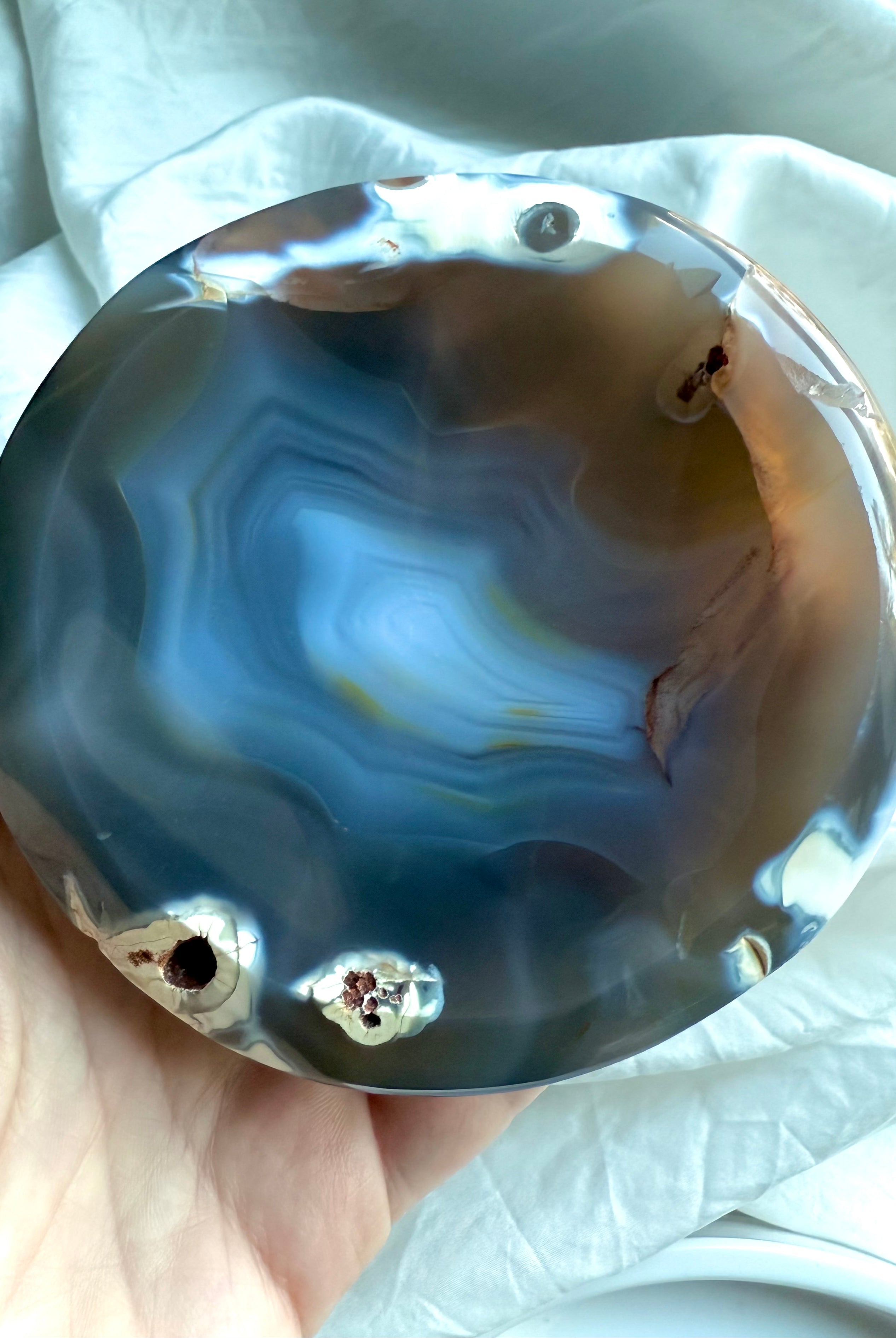 Hand holding glossy Orca Agate bowl showing soothing blue-grey banding and natural druzy pockets for forgiveness work