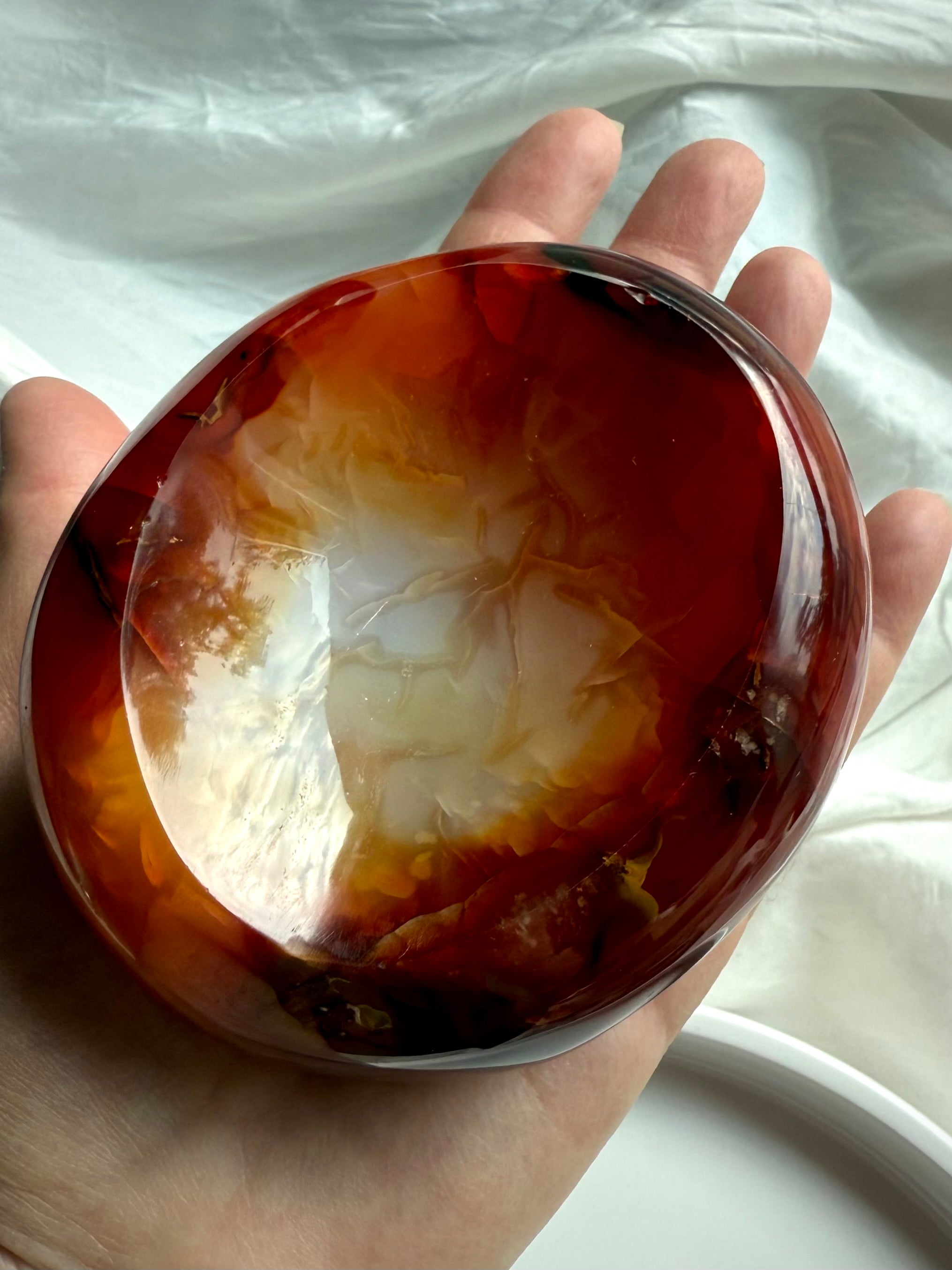 Hand holding Carnelian crystal bowl, displaying polished interior with fiery red and white banded patterns.