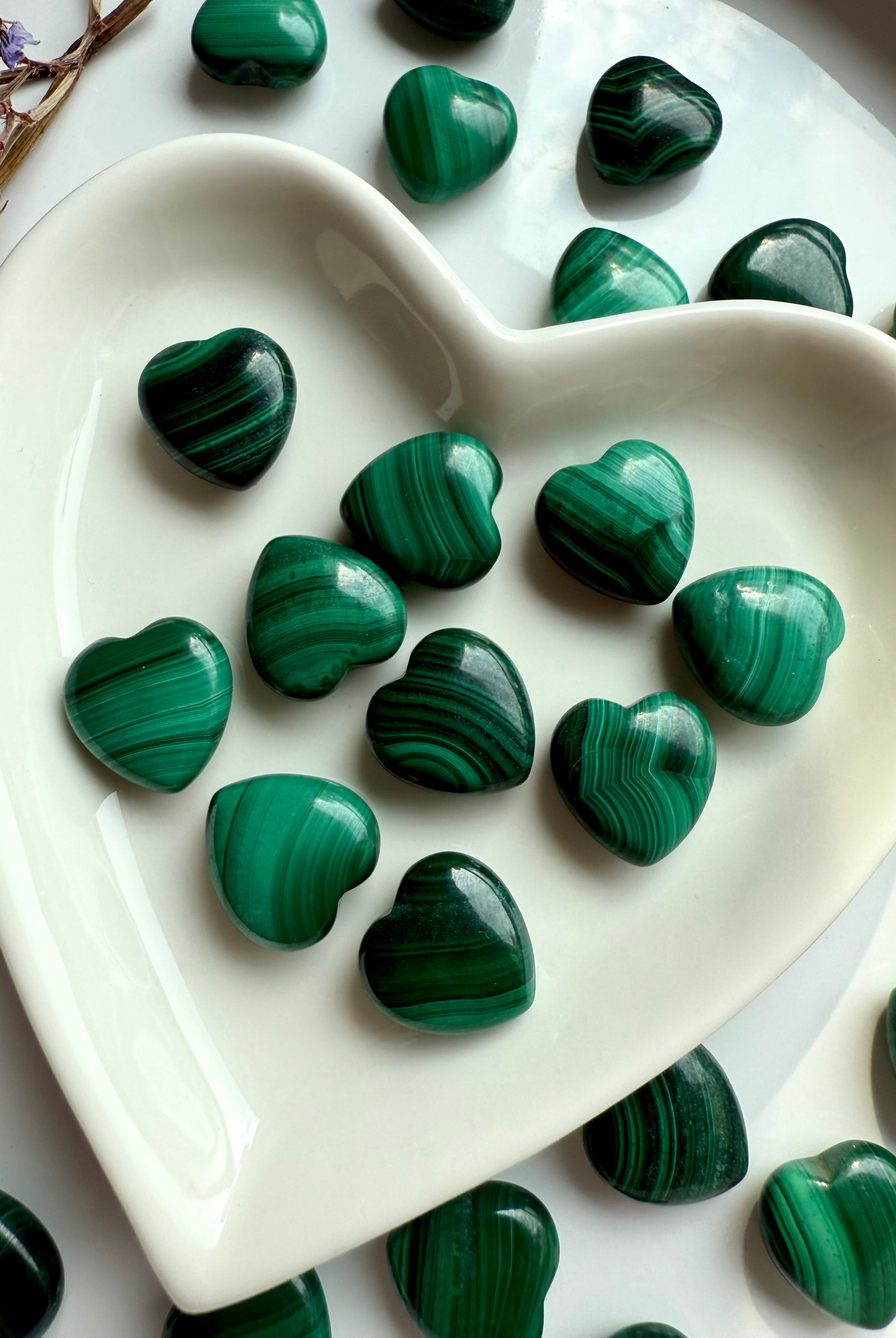 Detail view of polished Mini Malachite hearts in white heart bowl showcasing layered greens, bubbles, and chatoyant texture