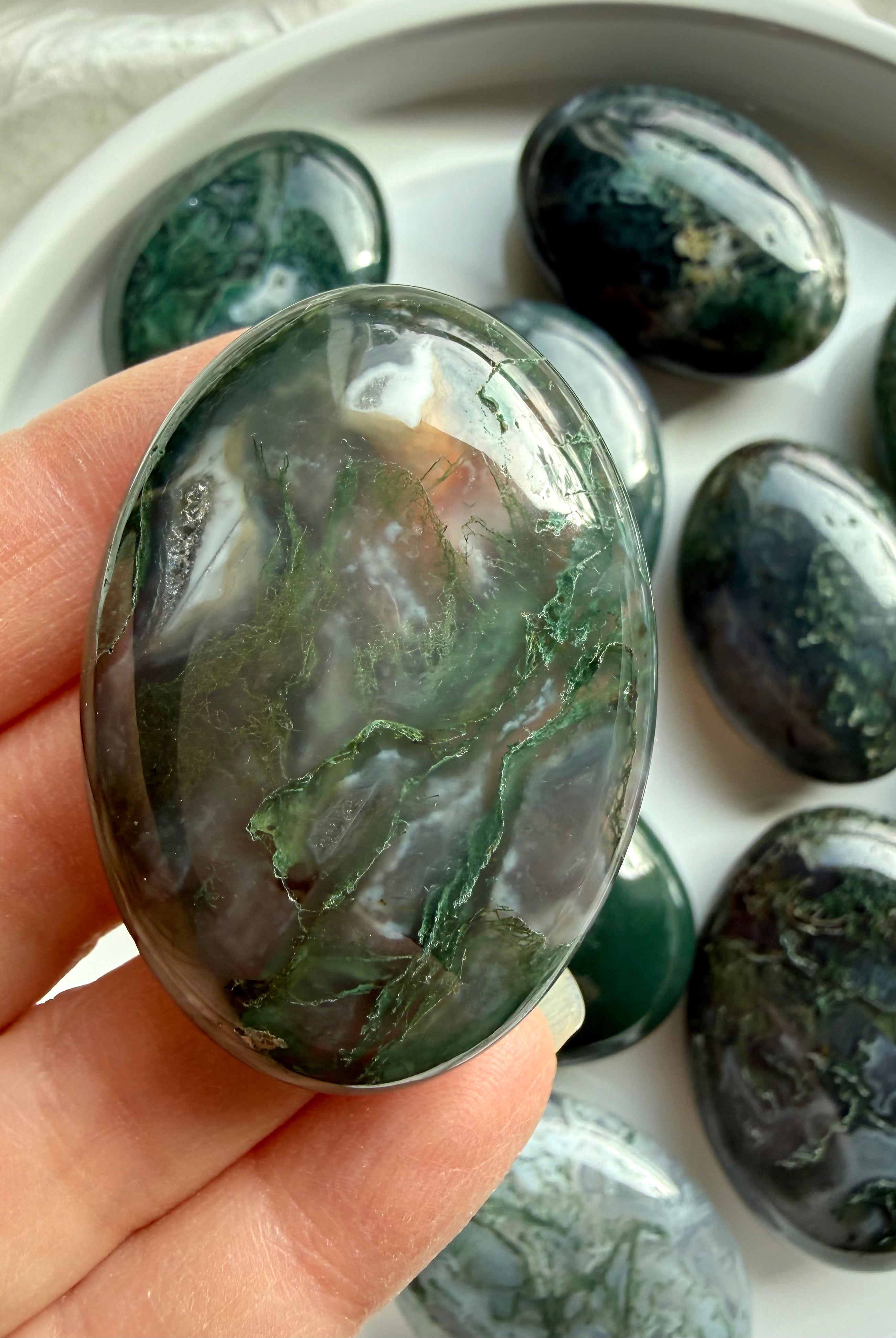 Polished moss agate palm stone resting in palm, earthy green crystal for emotional balance and grounding energy