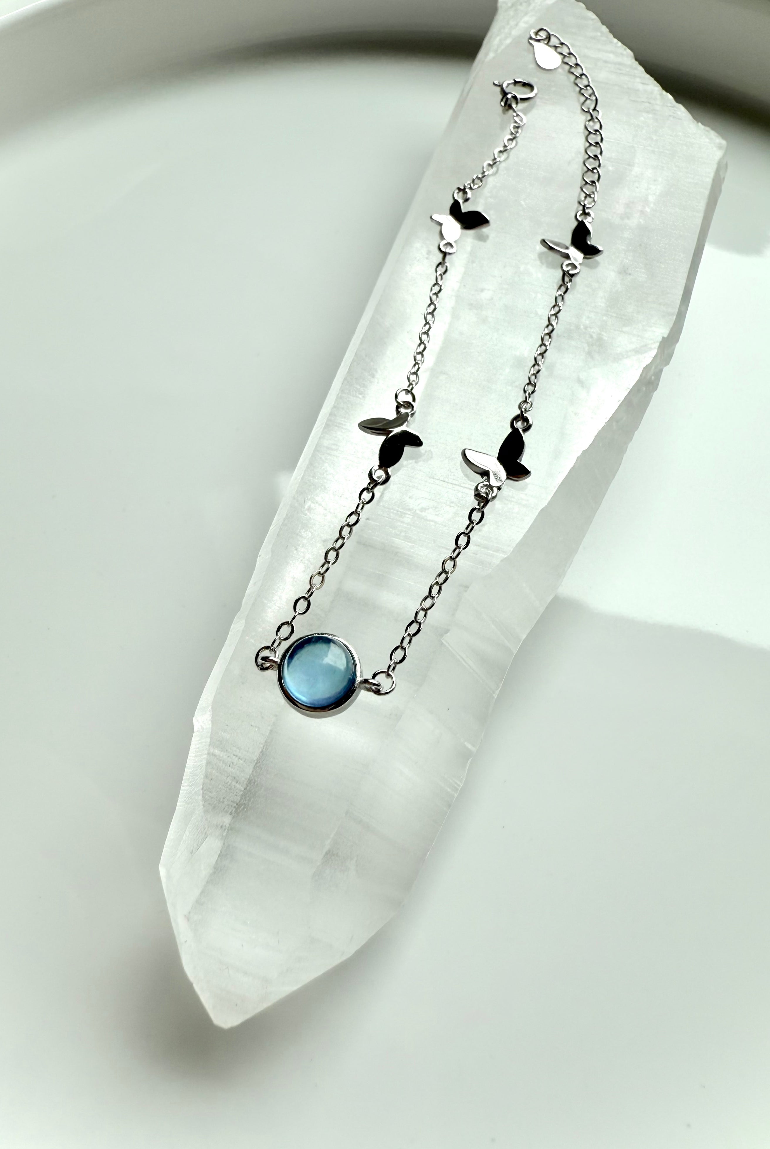 Aquamarine gemstone bracelet with silver butterfly charms displayed on a Lemurian Quartz wand for spiritual healing and clarity