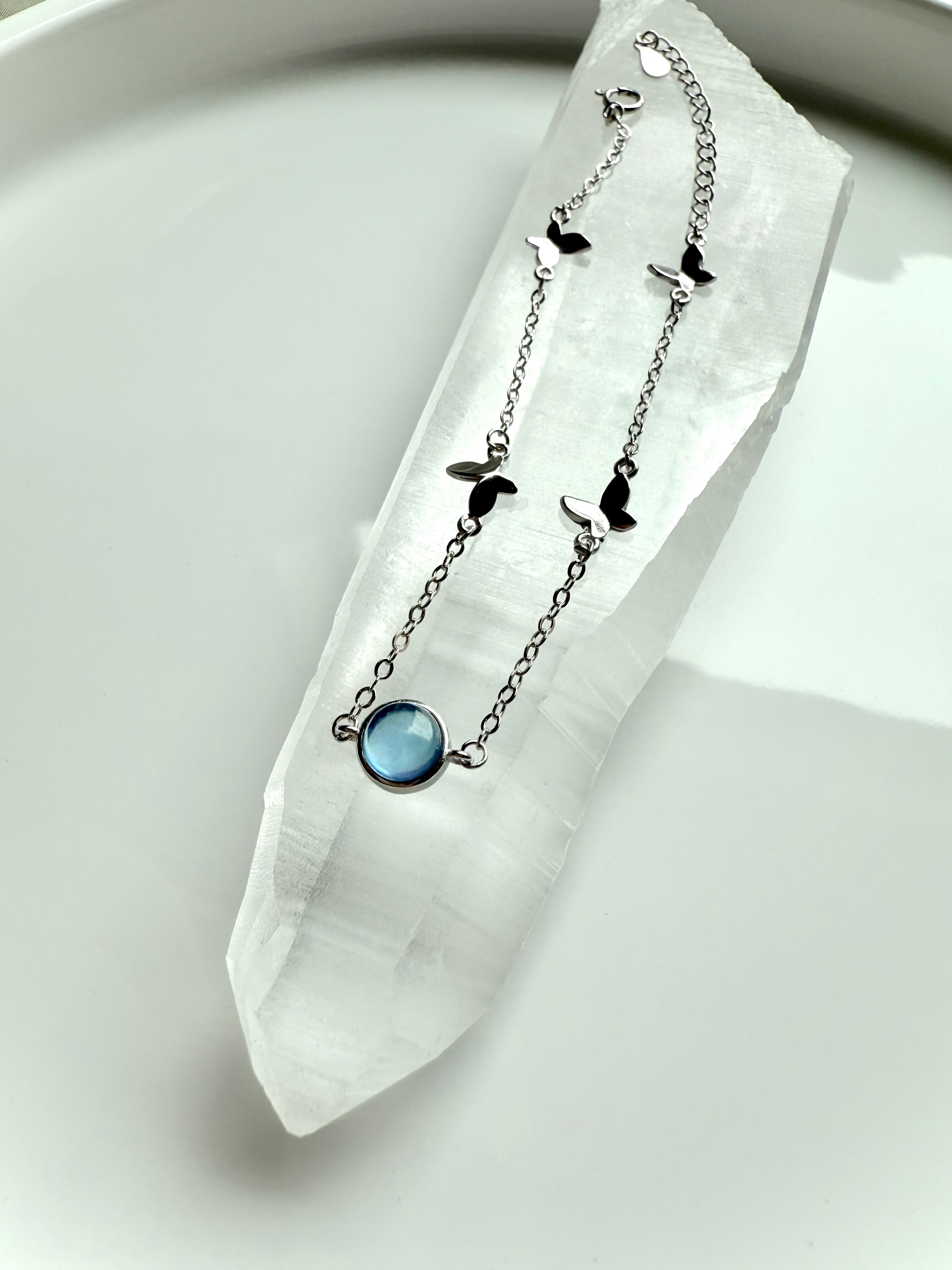 Aquamarine gemstone bracelet with silver butterfly charms displayed on a Lemurian Quartz wand for spiritual healing and clarity