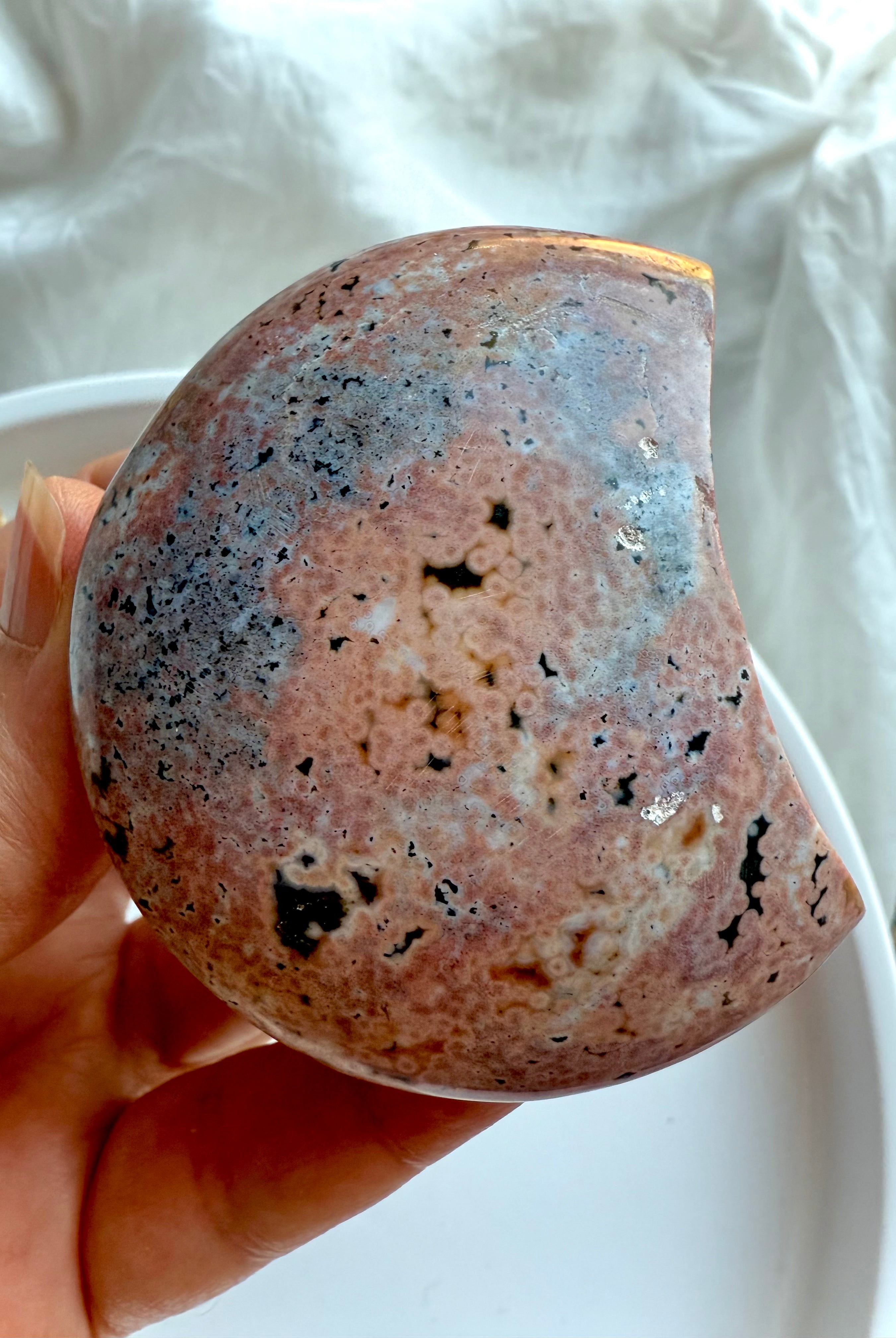 soft pink and grey ocean jasper moon with natural orbs and inclusions shown in hand, calming gemstone for emotional release and gentle grounding