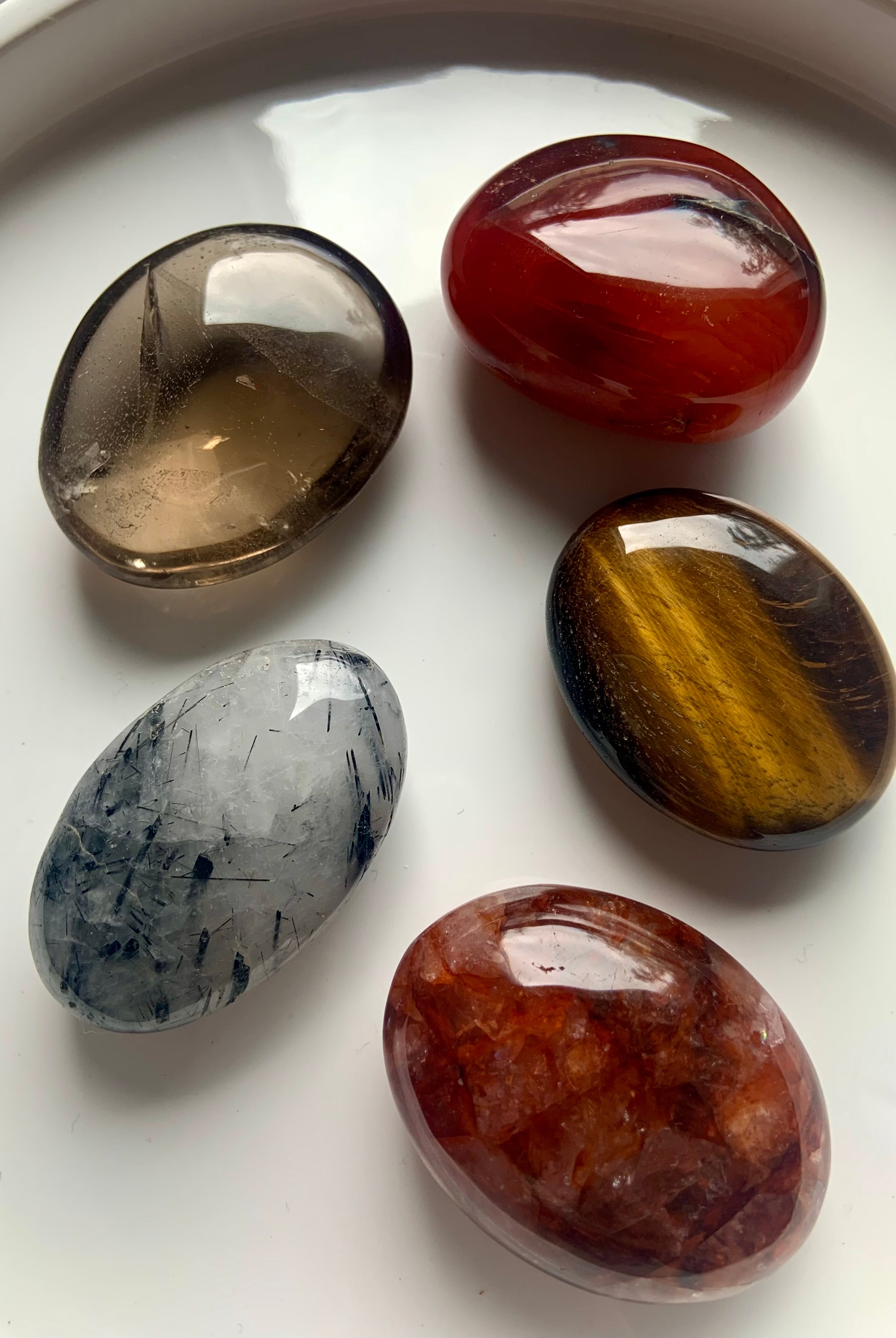 Root, Sacral + Solar Plexus Chakra crystal palm stone set on white plate — includes Smokey Quartz, Tigers Eye, Carnelian, Fire Quartz & Tourmaline in Quartz.