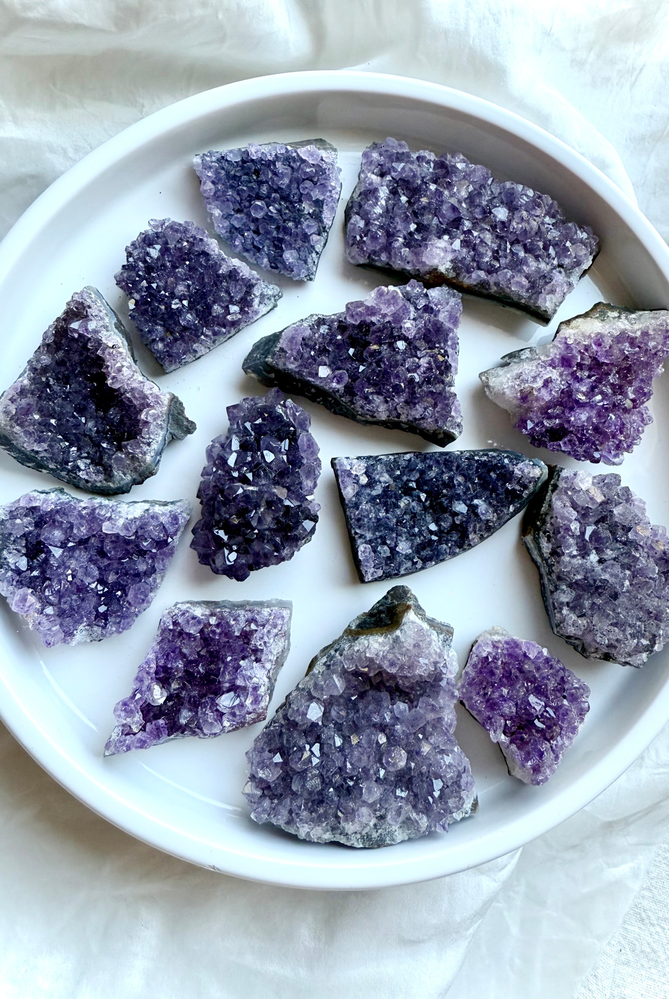 Purple Amethyst geode clusters in assorted sizes displayed on a white plate