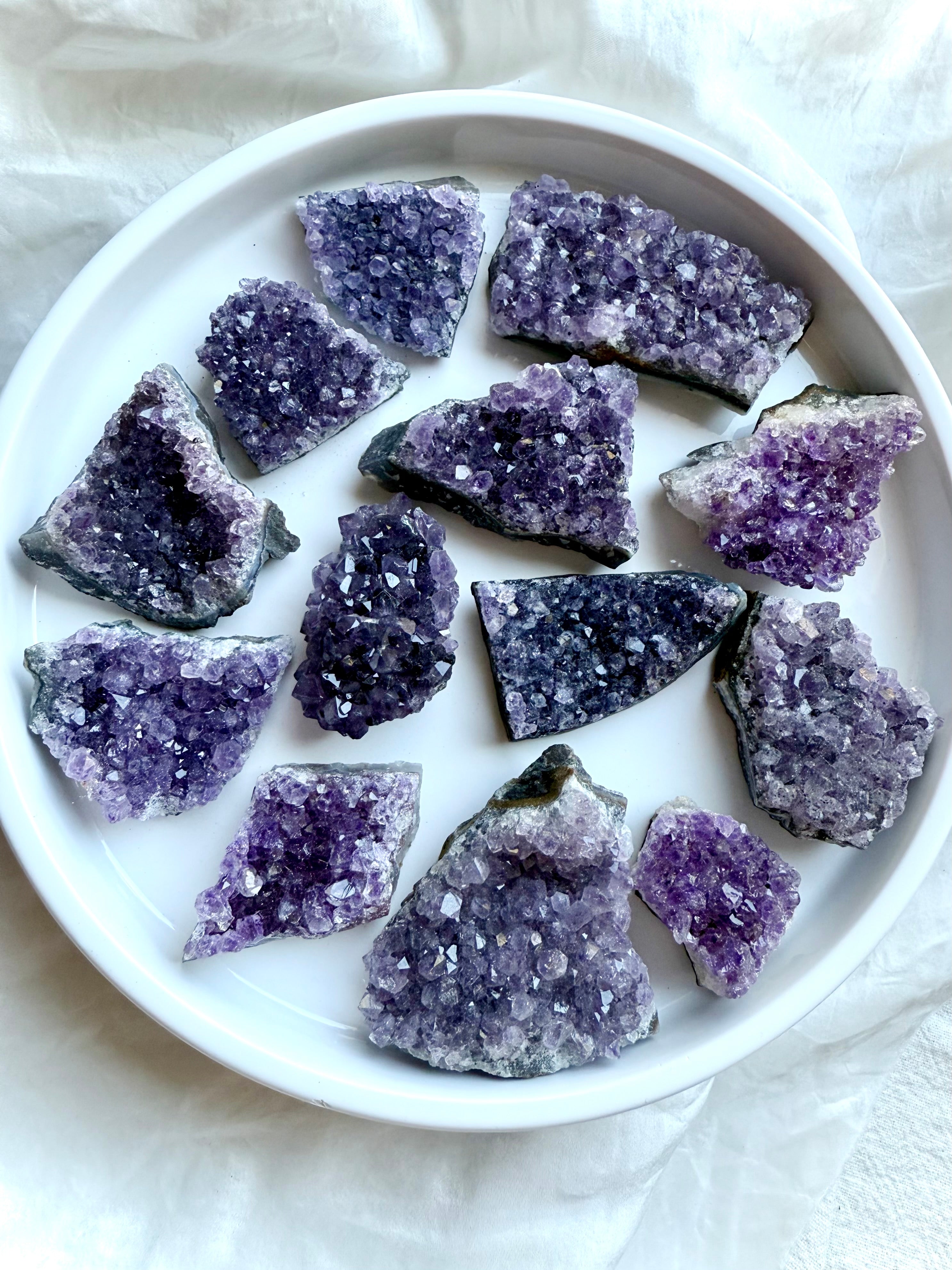 Purple Amethyst geode clusters in assorted sizes displayed on a white plate