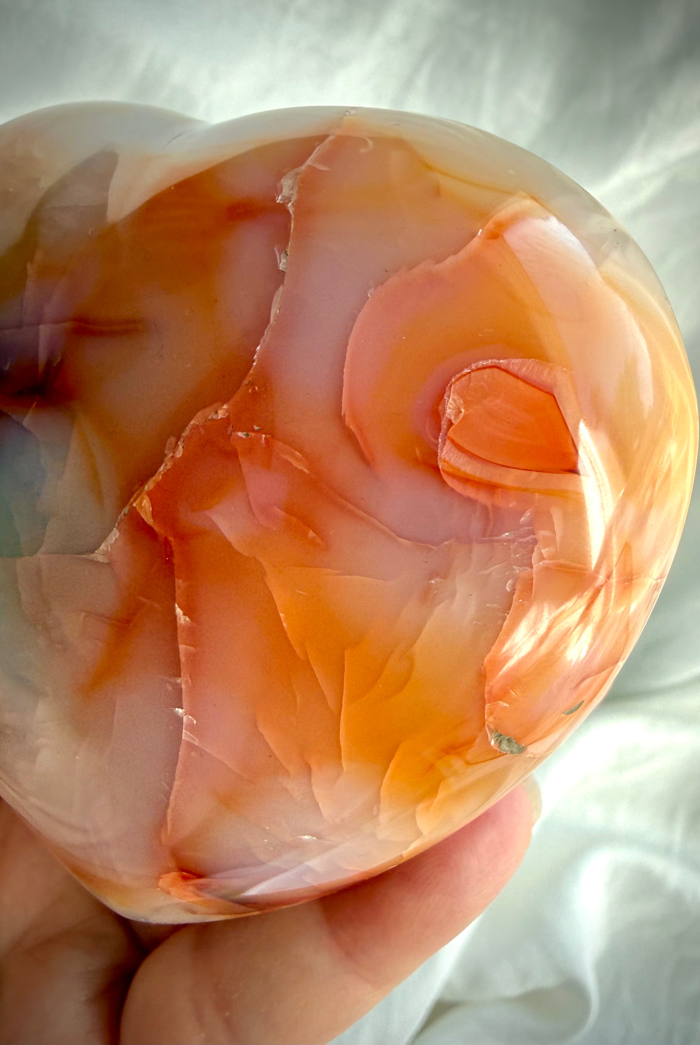 Close- up angle of a polished Carnelian heart showing flowing orange and golden mineral patterns in natural light