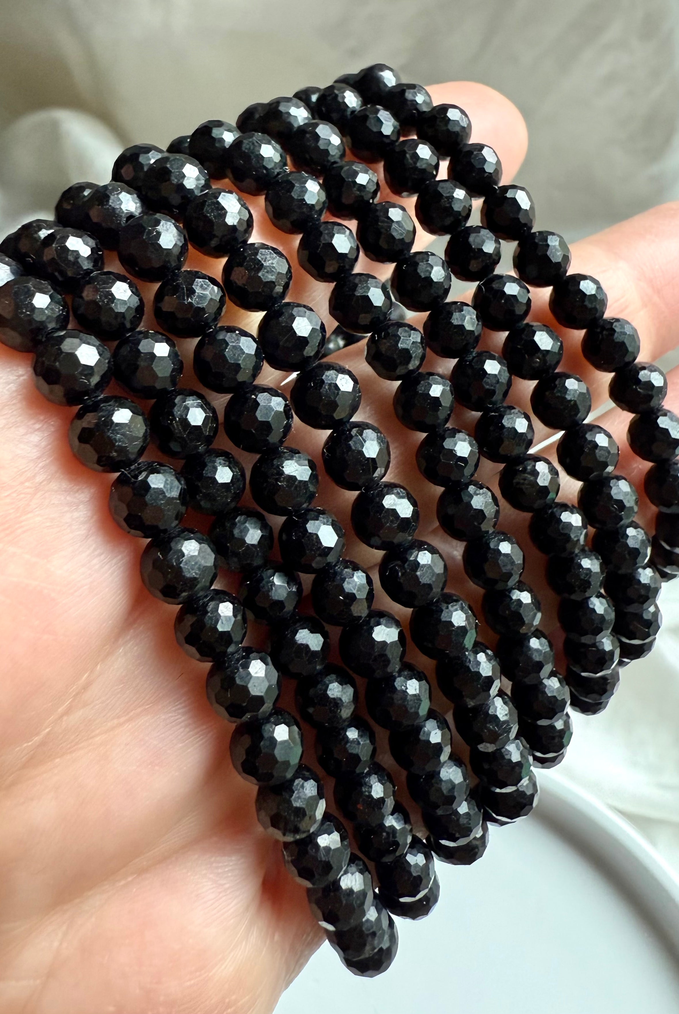 close-up of faceted black tourmaline crystal bracelets stacked in hand, showcasing high-shine polish and protective grounding energy