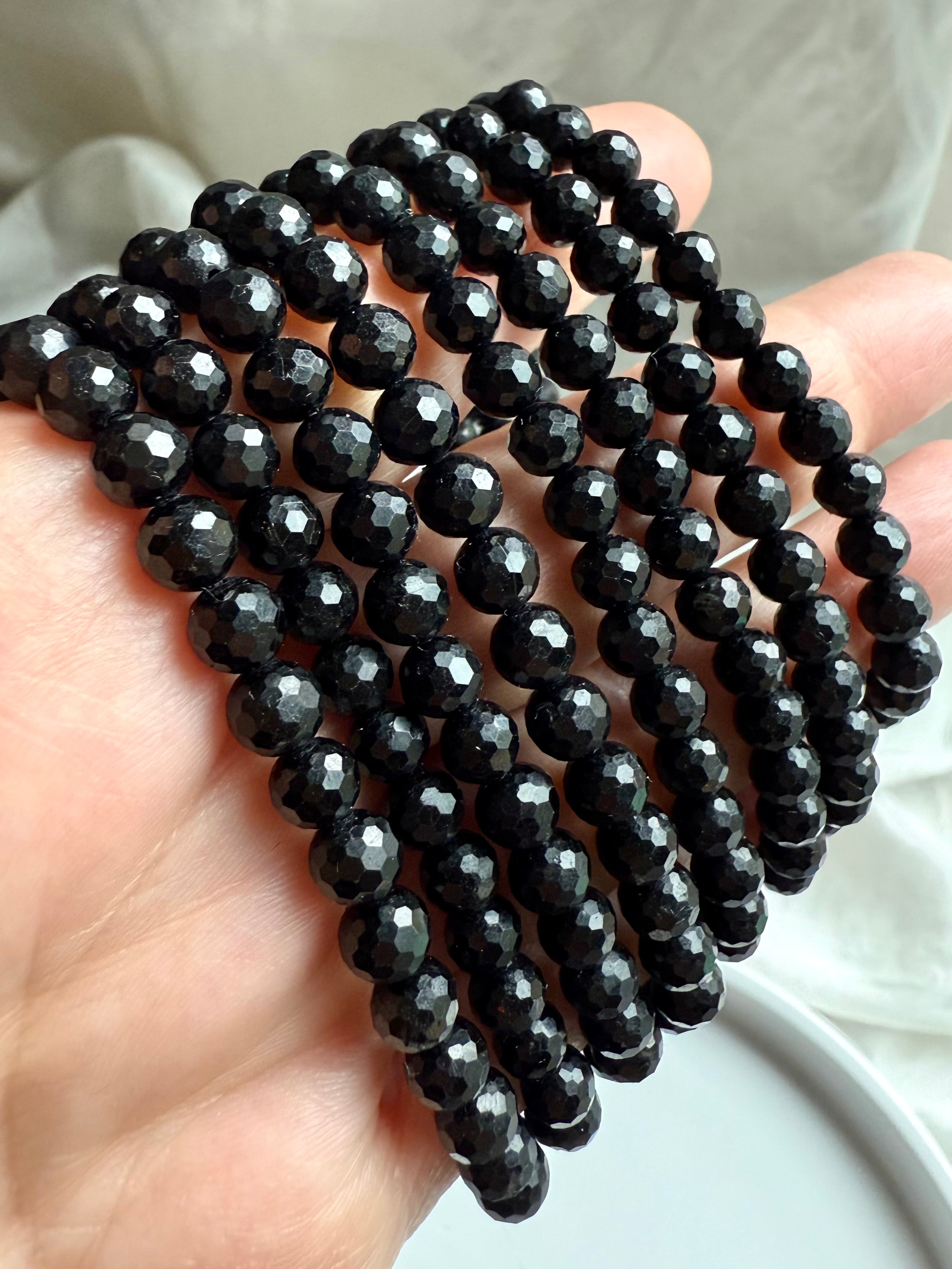 close-up of faceted black tourmaline crystal bracelets stacked in hand, showcasing high-shine polish and protective grounding energy