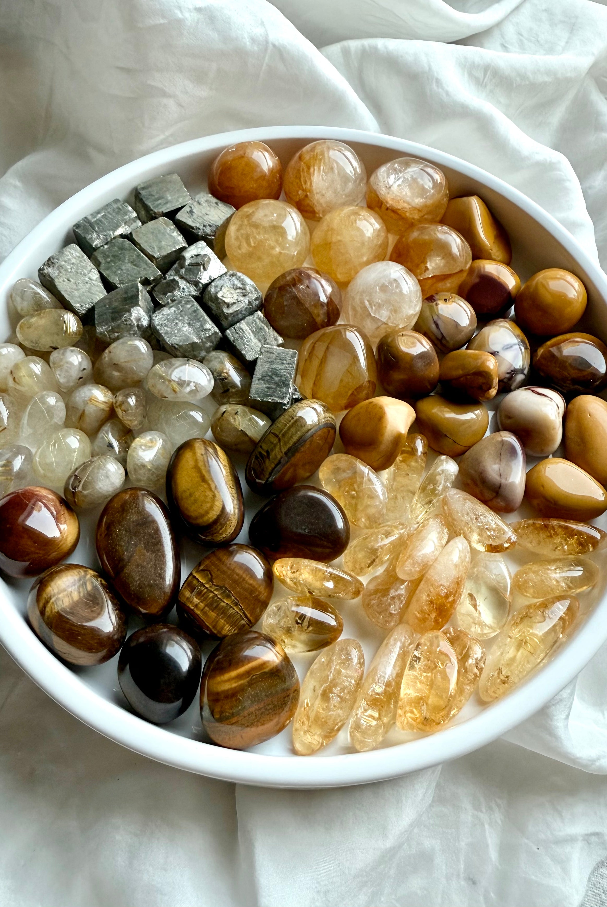 Wide view of chakra crystal set in pie-slice formation — solar plexus stones including golden healer, citrine, rutile, tiger’s eye, mookaite, and raw pyrite on white plate