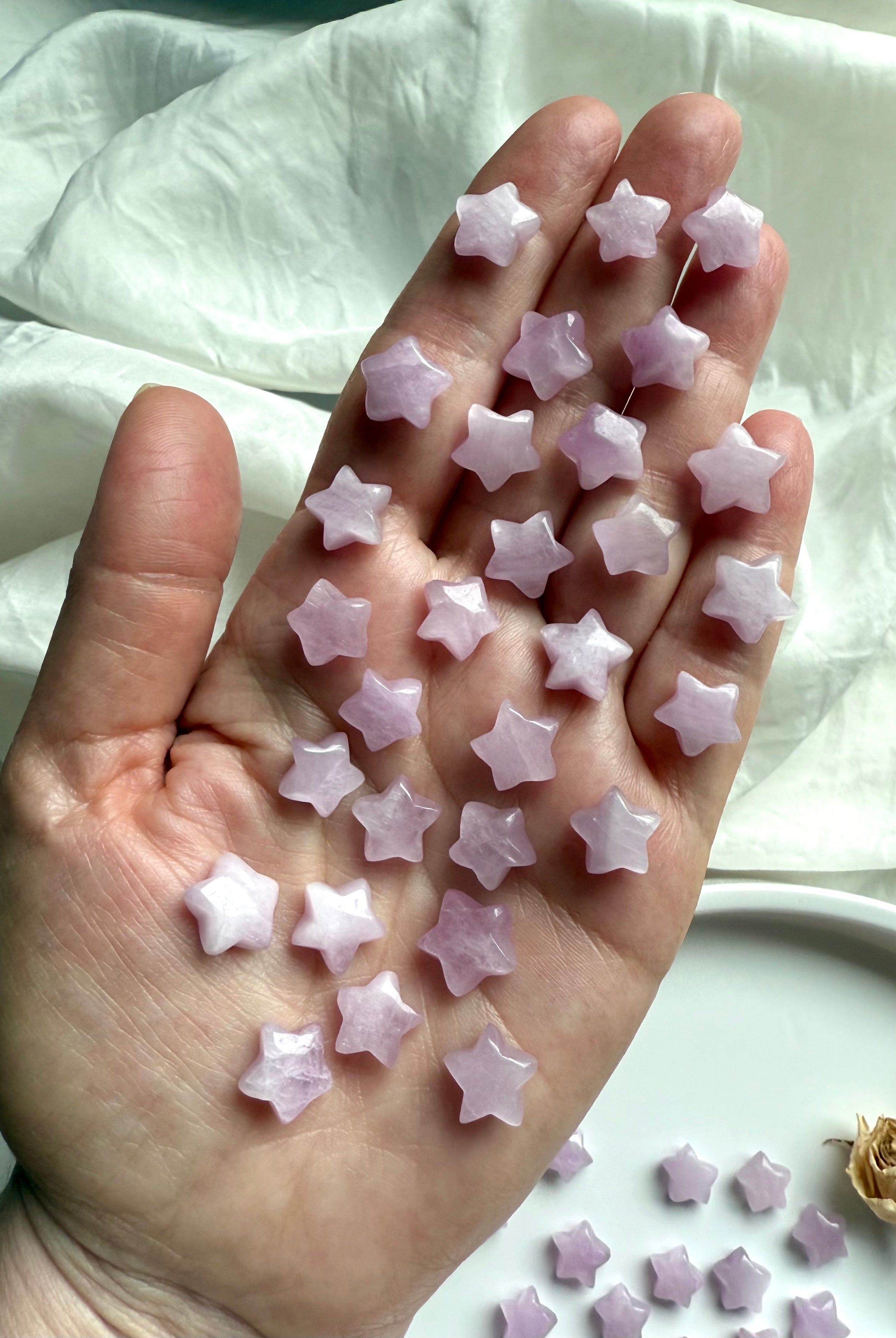 Hand holding many small Kunzite stars to show size and sparkle — miniature crystal star carvings for heart chakra energy work.