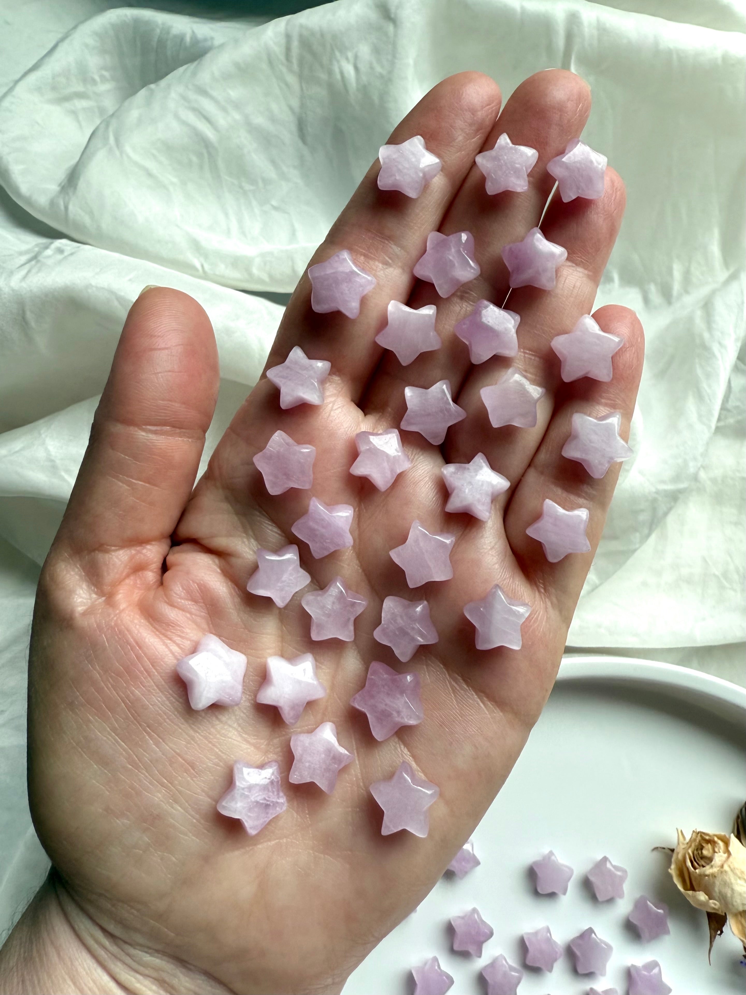 Hand holding many small Kunzite stars to show size and sparkle — miniature crystal star carvings for heart chakra energy work.