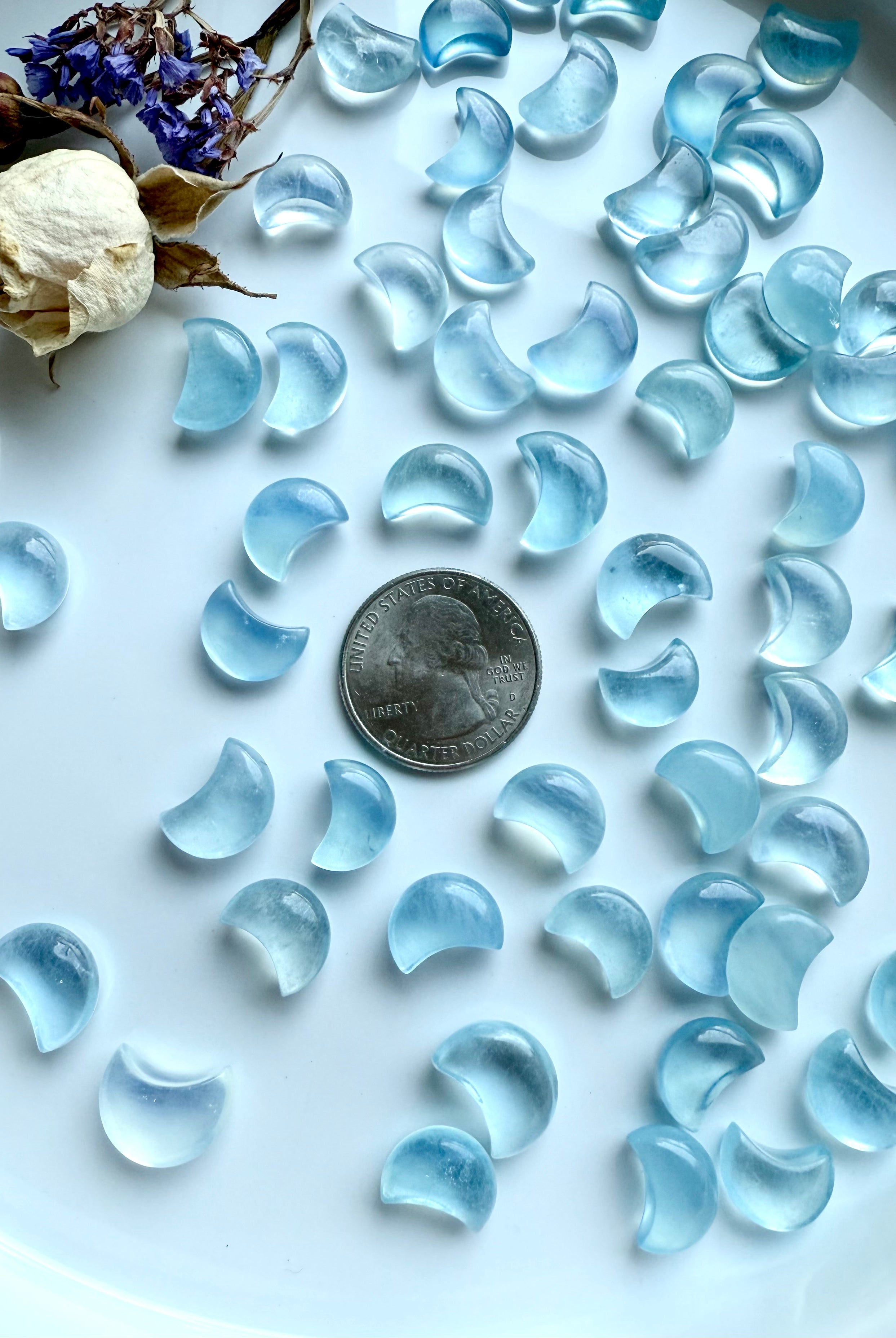 Aquamarine crystal moons surrounding a US quarter for size reference — tiny crescent carvings for crystal grids and moon rituals