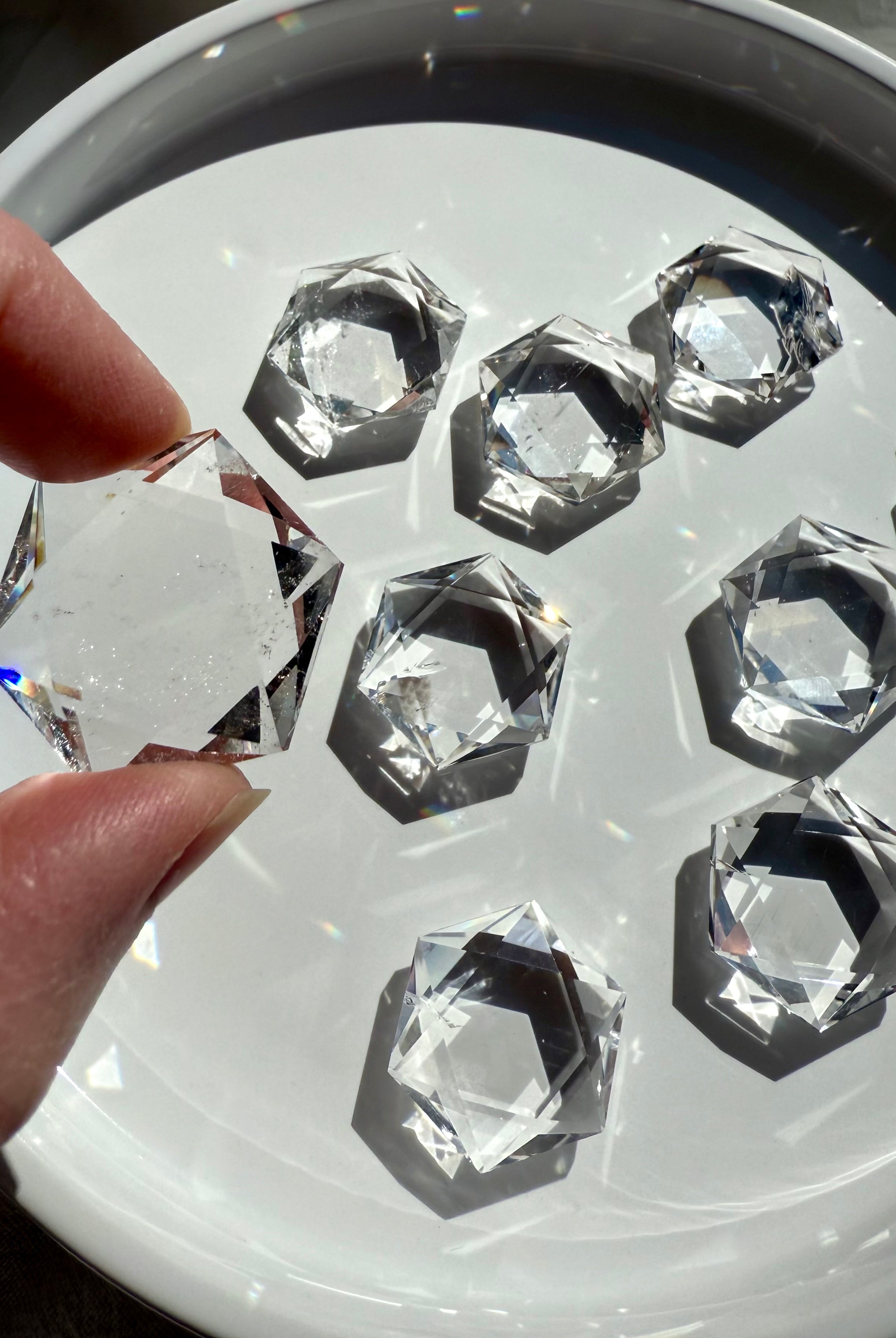 Overhead of plate full of Clear Quartz hexagons in bright sunlight, reflective facets sparkling with one held in foreground
