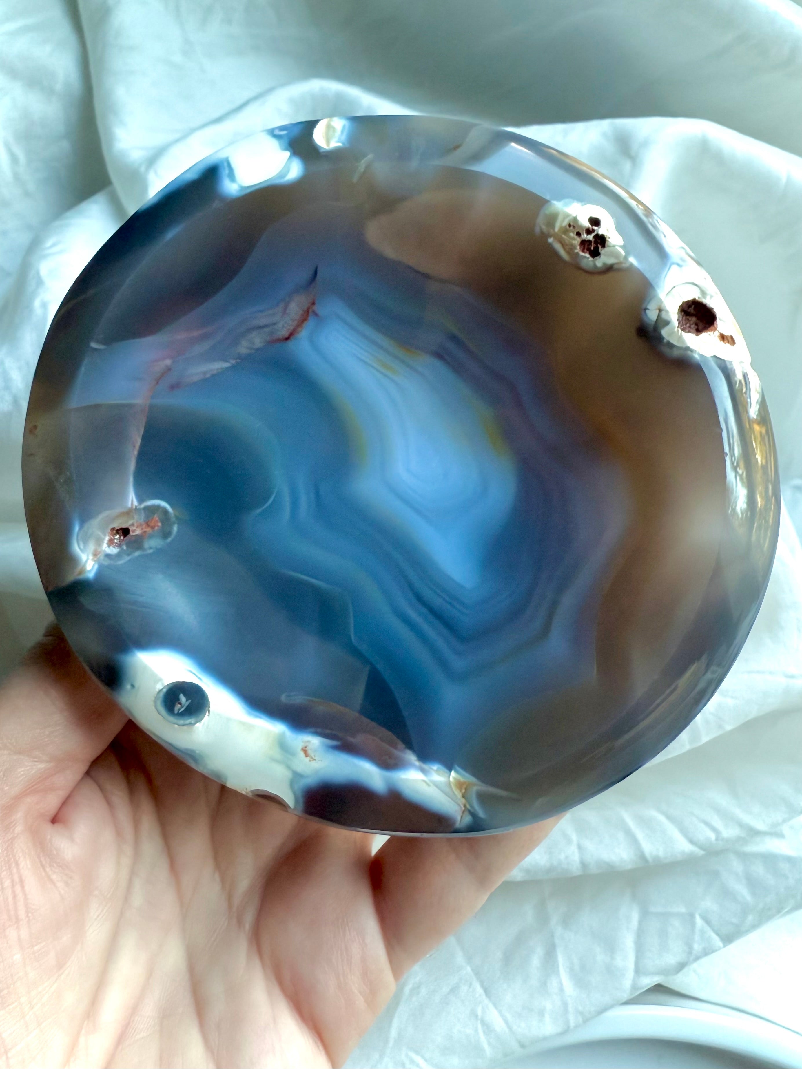 Hand holding polished Orca Agate bowl showing swirling blue, grey, and cream banding for emotional healing