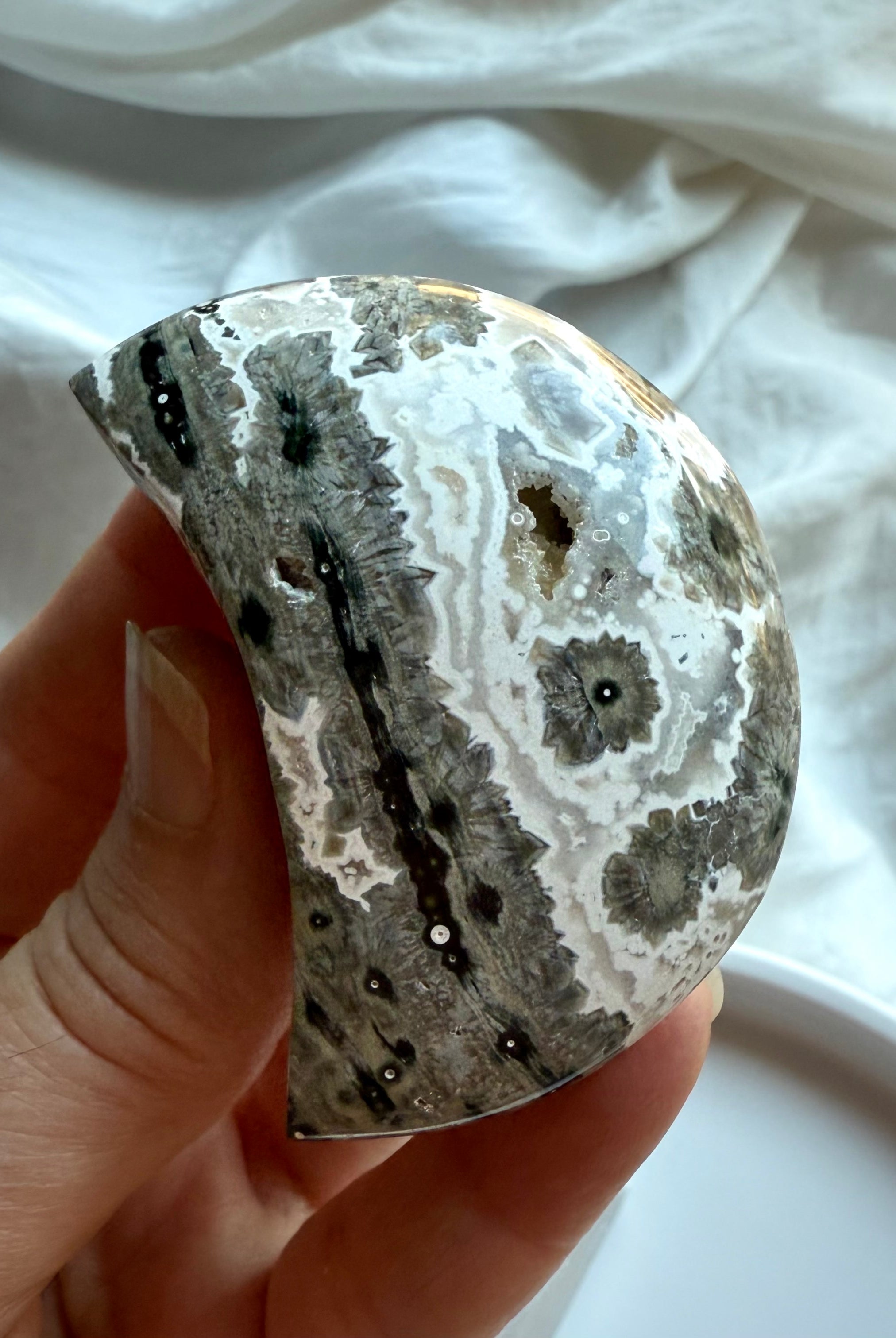 Polished Ocean Jasper crescent moon in neutral gray tones with bold starburst orbs, calming stone for strength and stability