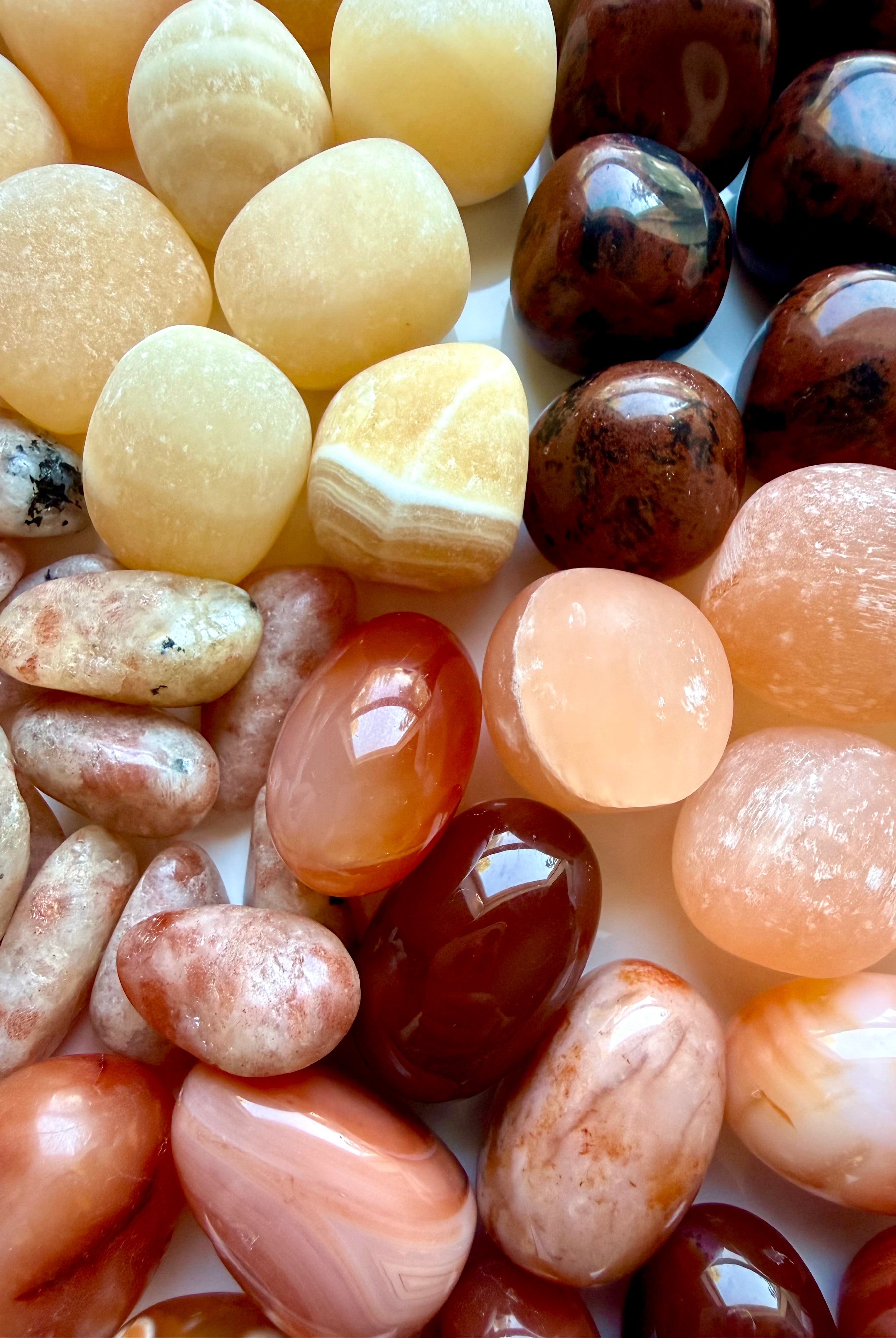 Close-up of polished Sacral Chakra stones in orange, peach, cream, and deep red with natural color and pattern variation