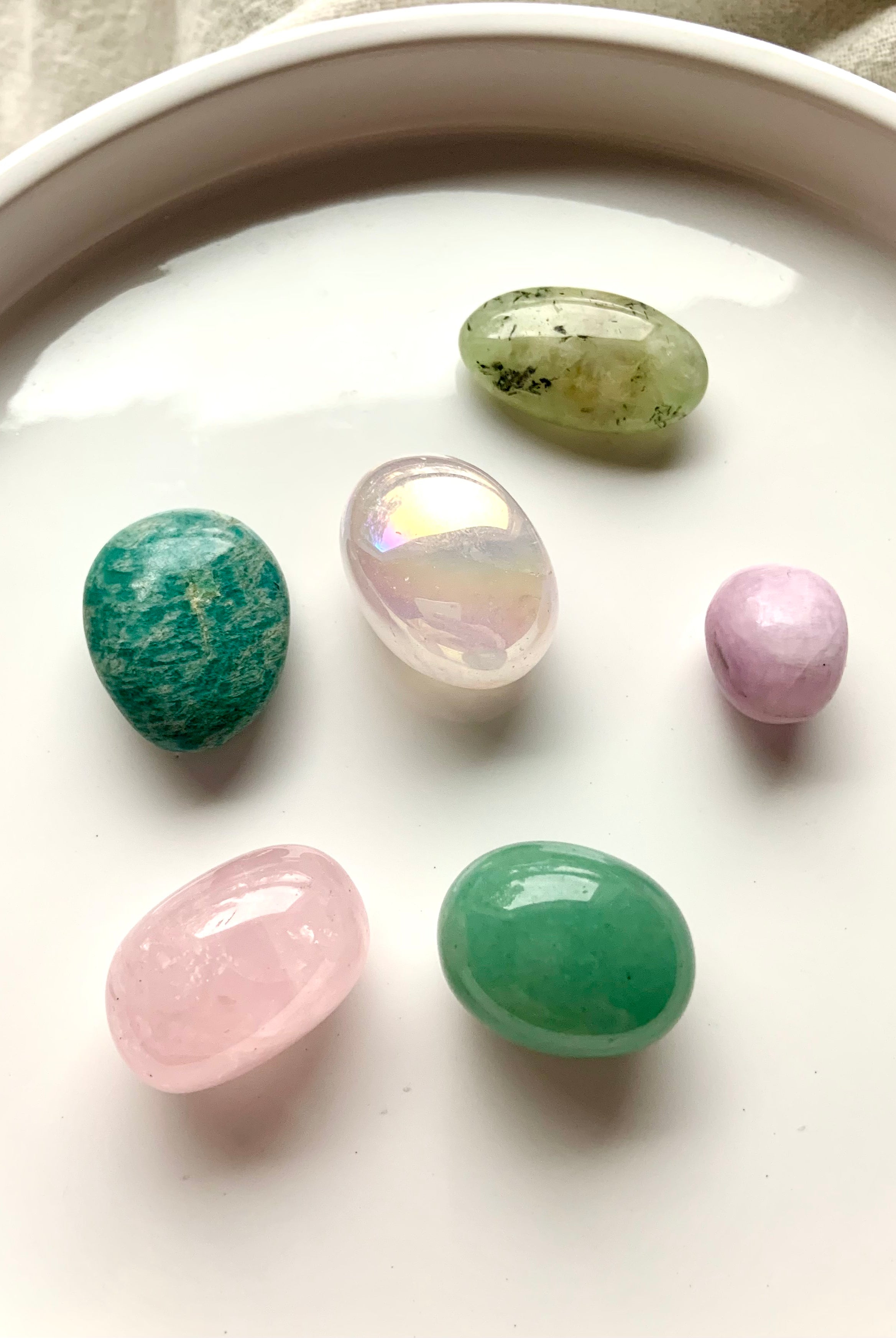 Heart Chakra healing stones set of 7 crystals arranged on a white plate — includes aura rose quartz, rose quartz, kunzite, amazonite, prehnite, and green aventurine.