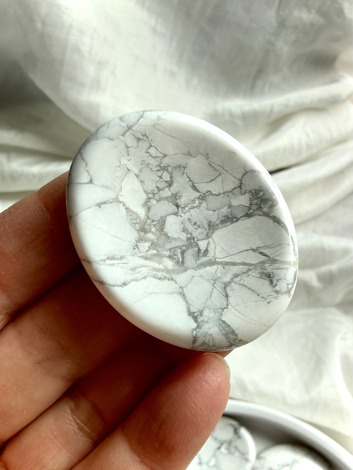 Natural Howlite worry stone held in hand showing unique white and gray marbled pattern and oval thumb stone shape