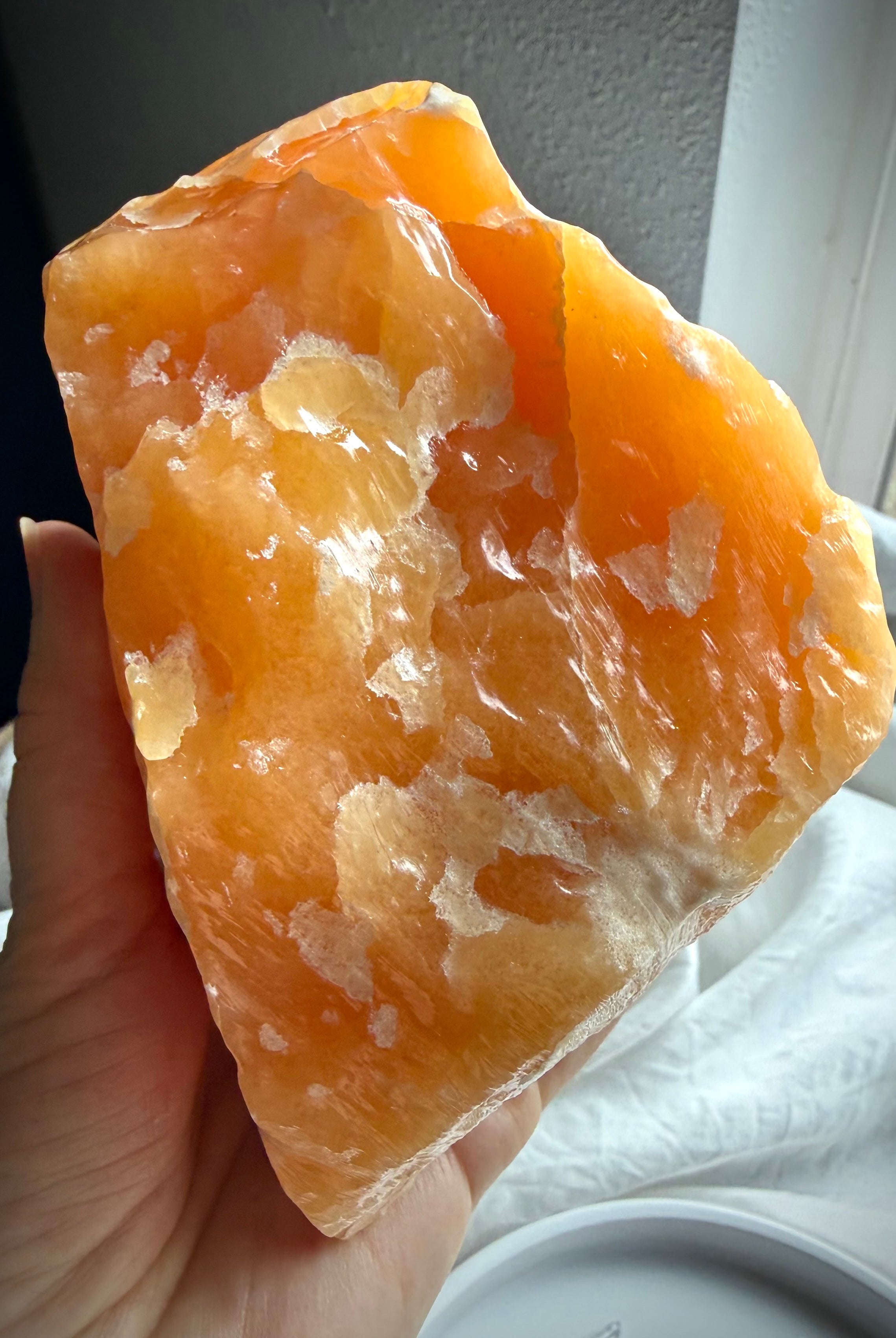 Handheld Orange Calcite mineral specimen showing natural texture, translucency, and layered formations