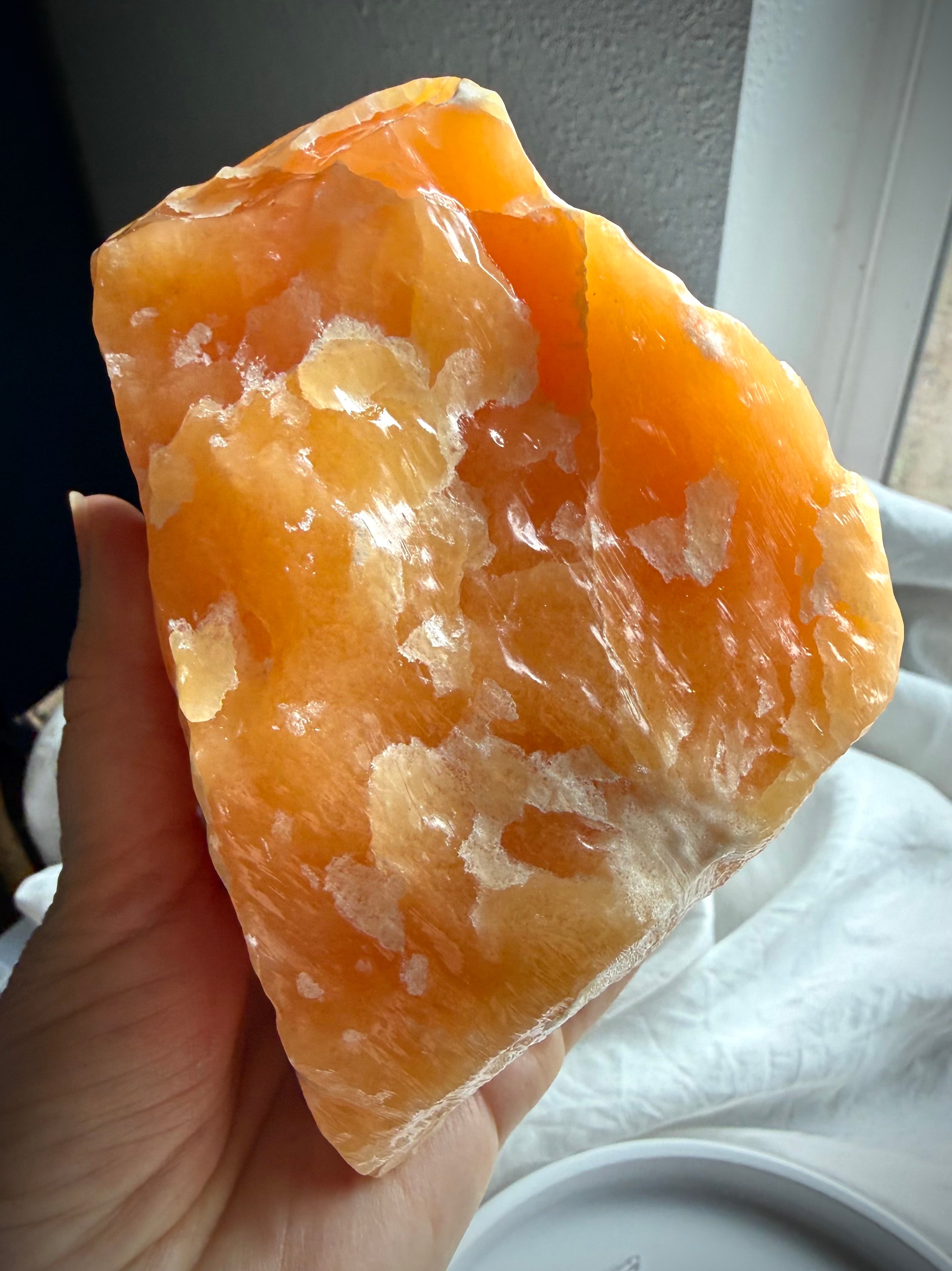 Handheld Orange Calcite mineral specimen showing natural texture, translucency, and layered formations
