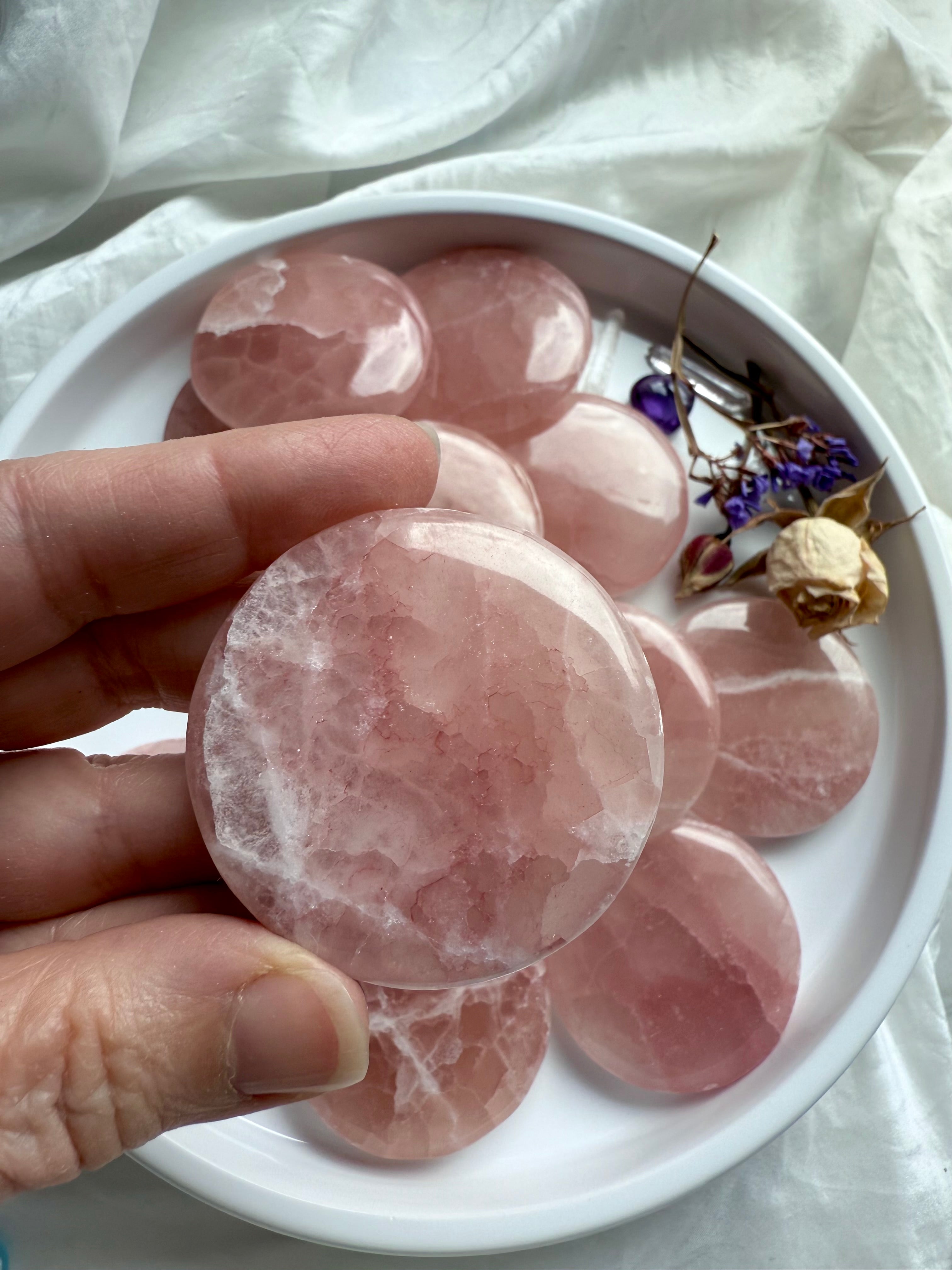 Close-up of a single Rose Calcite disc held above a plate full of pink crystals, highlighting translucent texture and white veining