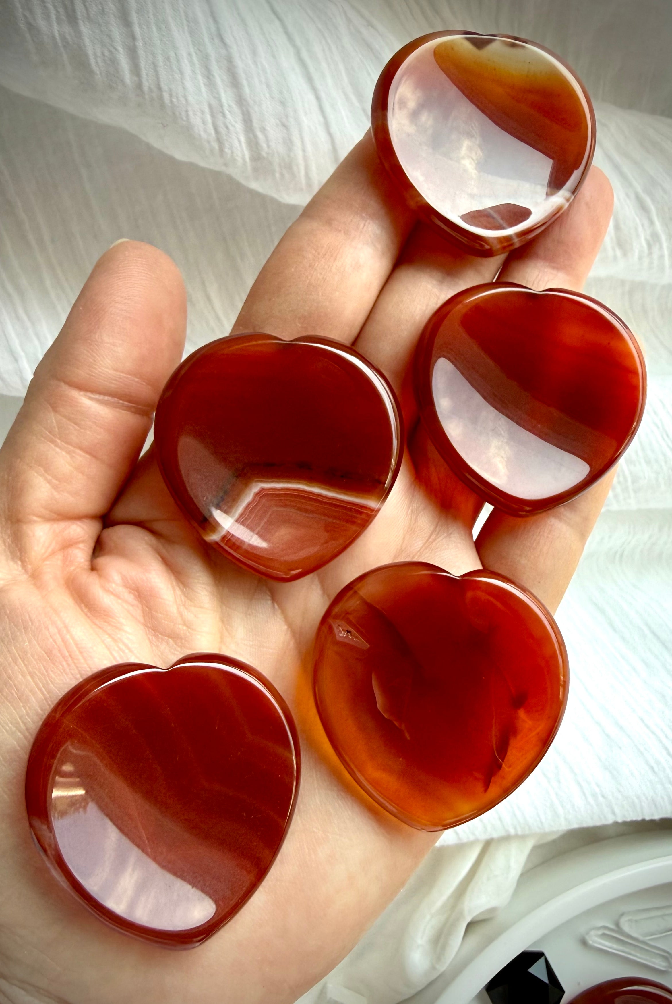 Carnelian heart worry stones held in hand showing glossy polish, rich red-orange color and natural translucent variation